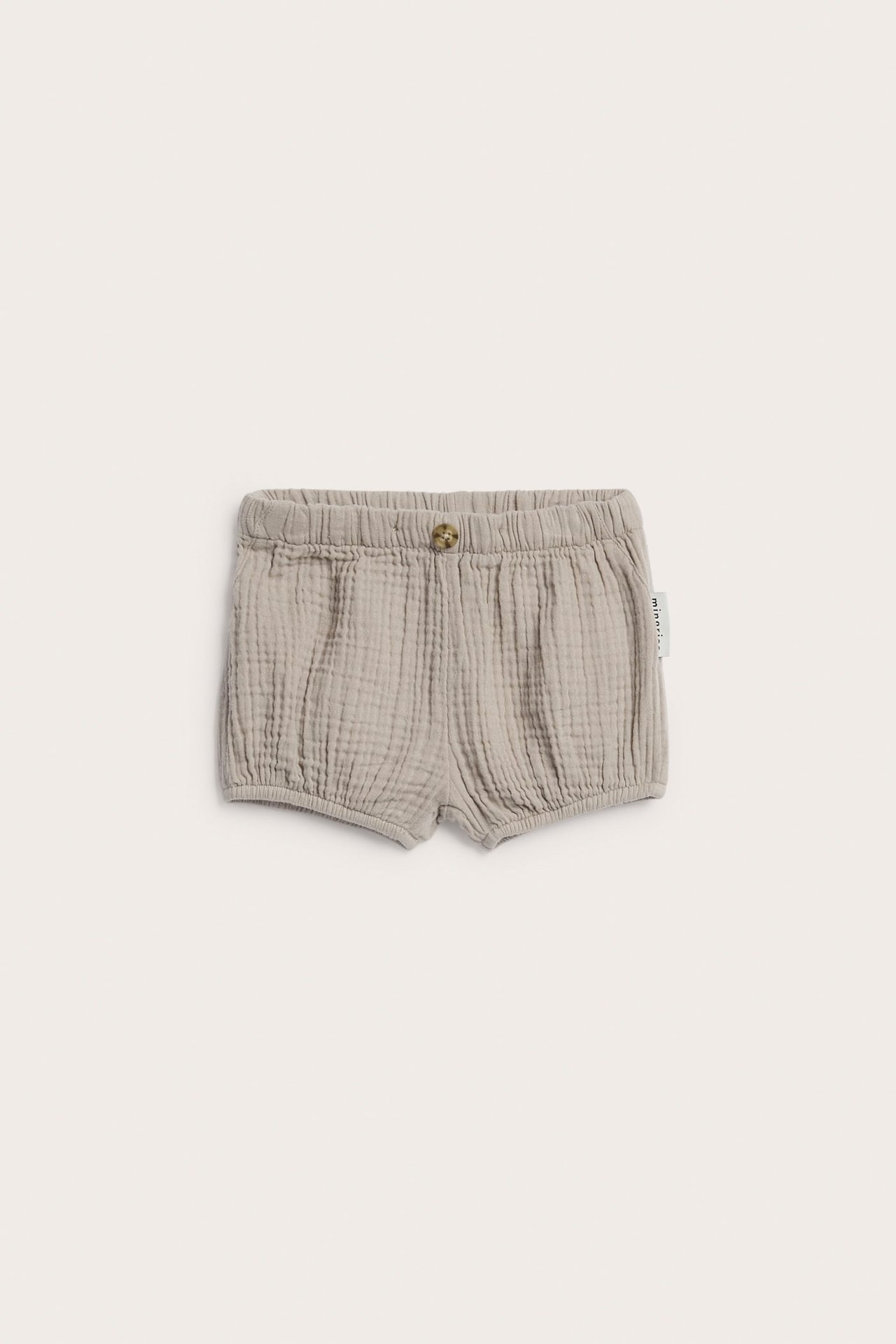 Frontbilde av beige vevde bomulls-babyshorts med elastisk linning og dekorativ knapp.