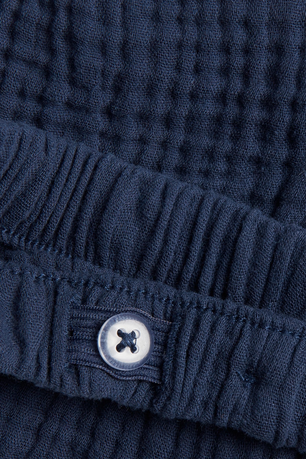 Zbliżenie na ciemnoniebieskie tkane szorty niemowlęce z elastyczną talią i białym ozdobnym guzikiem.