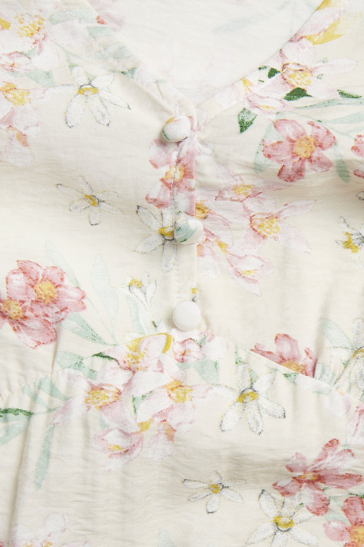 Nærbilde forfra av en lys beige blomstret kjole med V-hals og knapper foran.