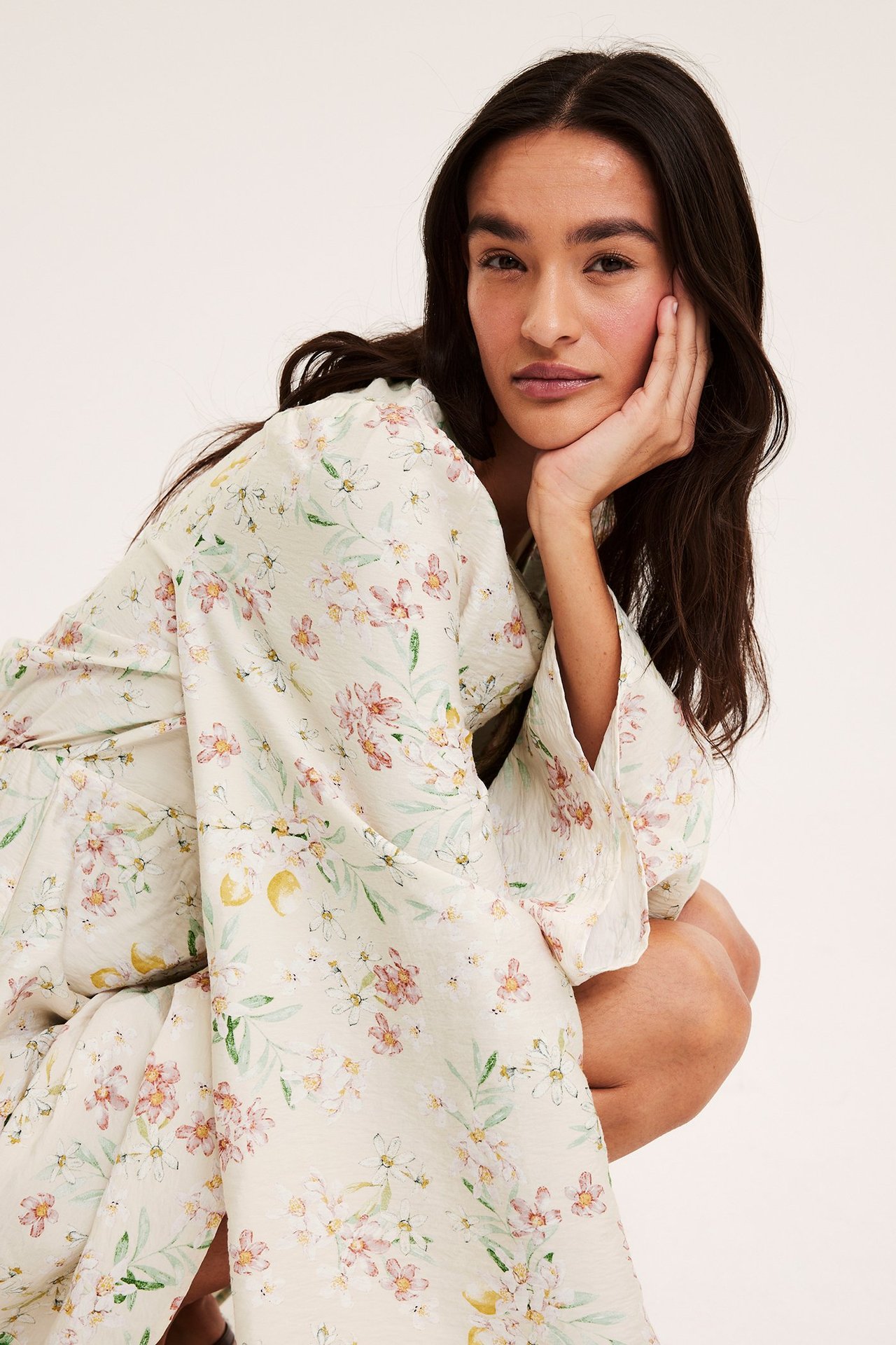 Nærbilde av en kvinne i en lys beige blomstret V-hals kjole med volangermer.