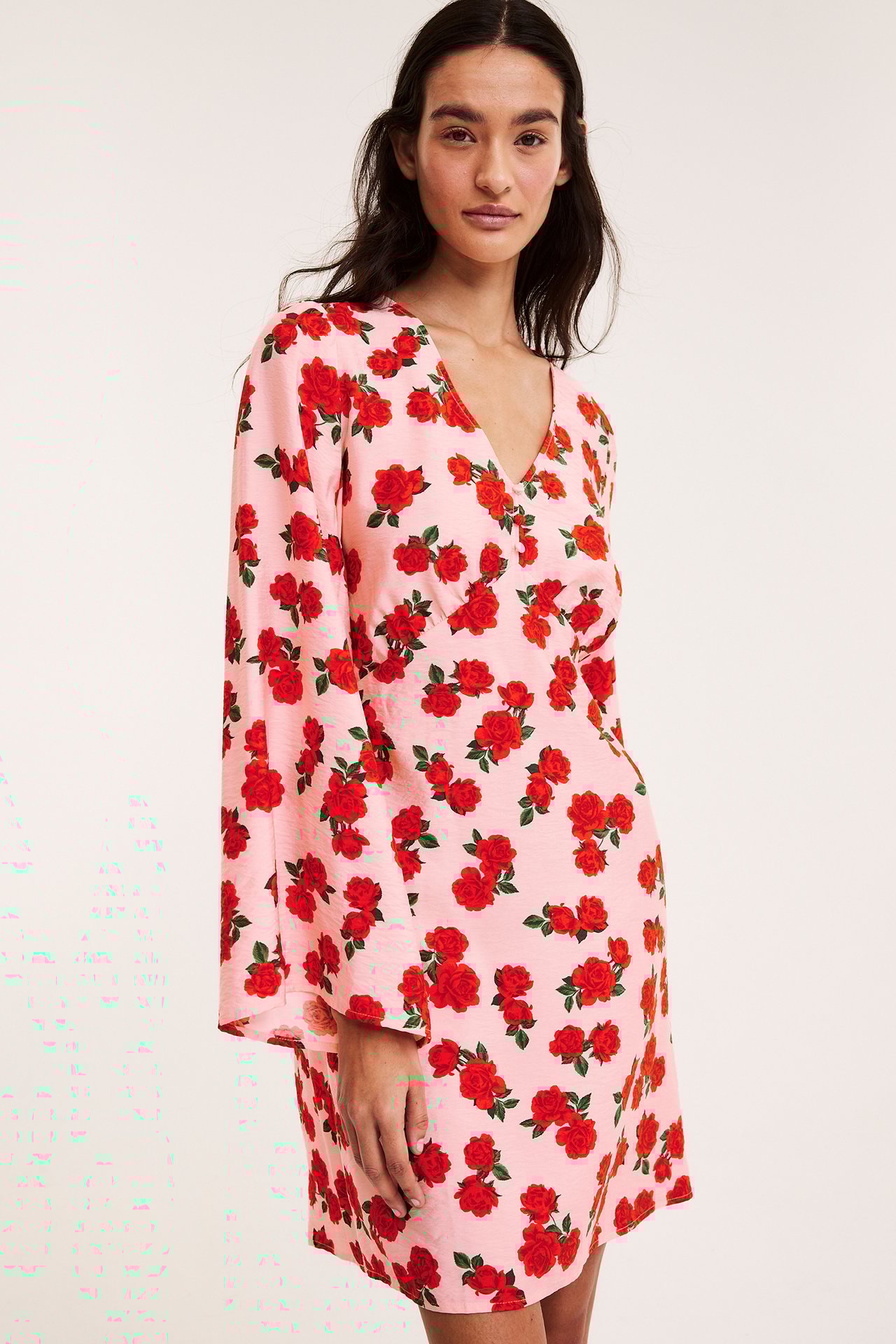 Framsida: Kvinna i ljusrosa klänning med röda rosor, V-ringning och långa volangärmar.