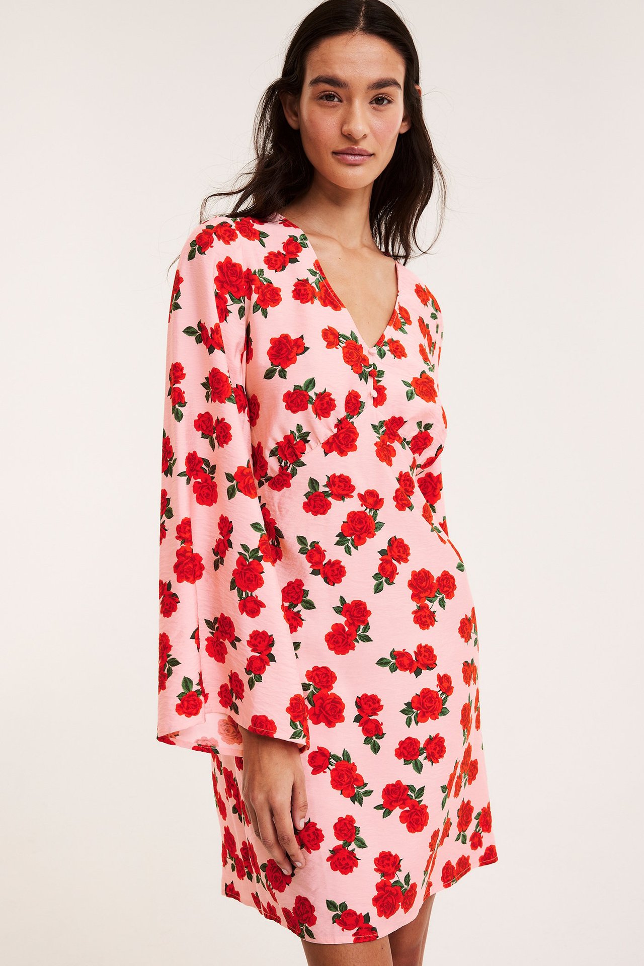 Frontutsikt: Kvinne i lyserosa kjole med røde roser, V-hals og lange volangermer.