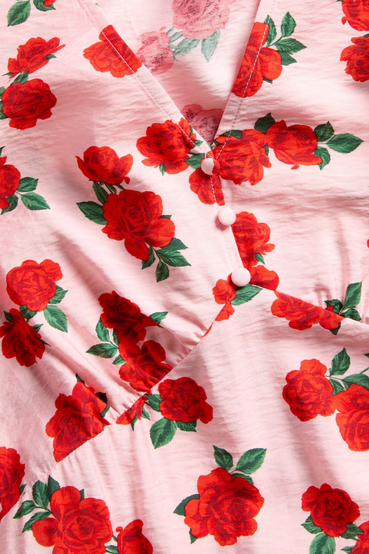 Närbild på en ljusrosa V-ringad klänning med rött rosmönster och rosa dekorativa knappar.