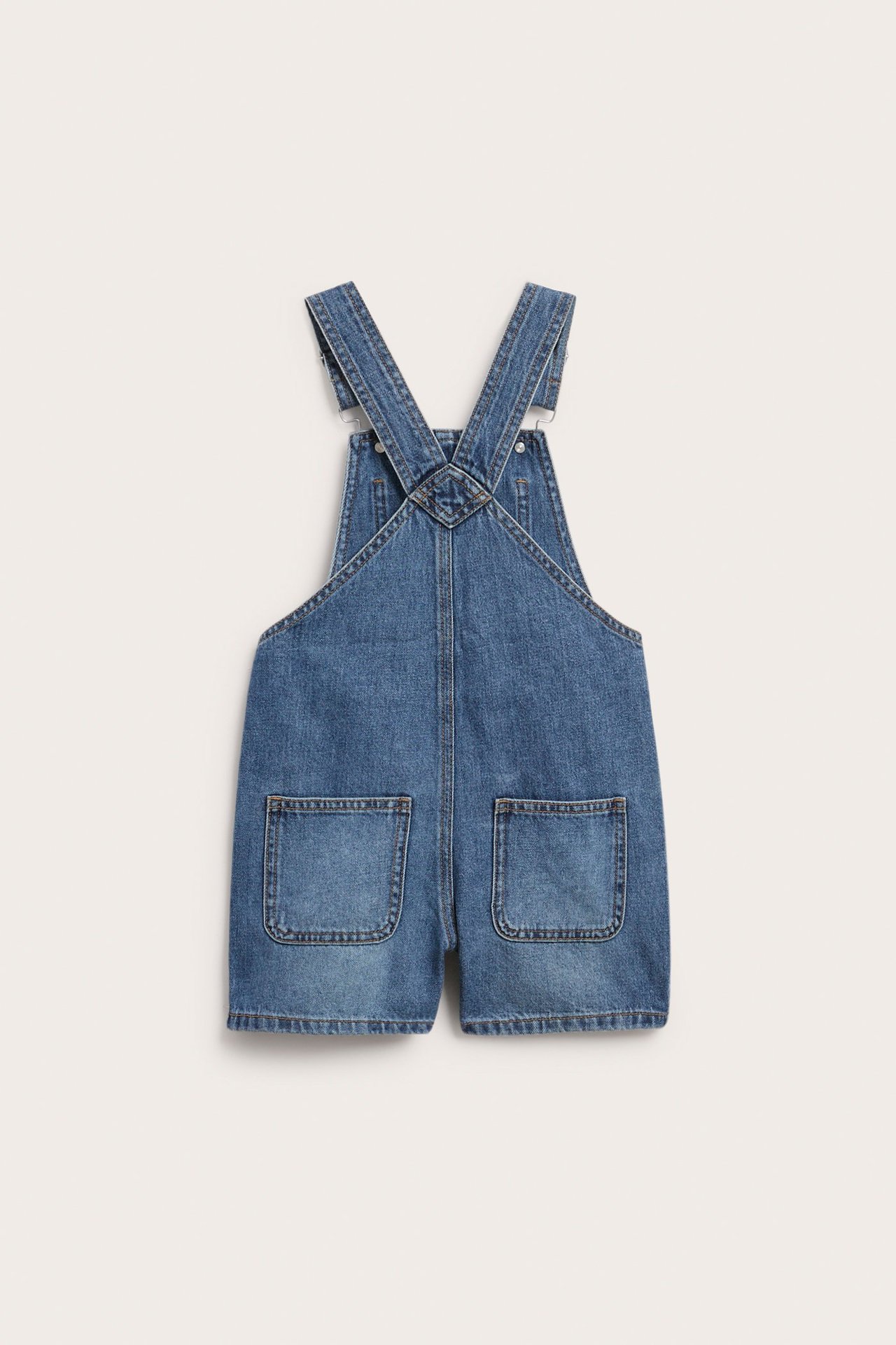 Takaa näkymä: denimpuuvillaiset haalarishortsit, joissa kaksi takataskua ja säädettävät olkaimet.