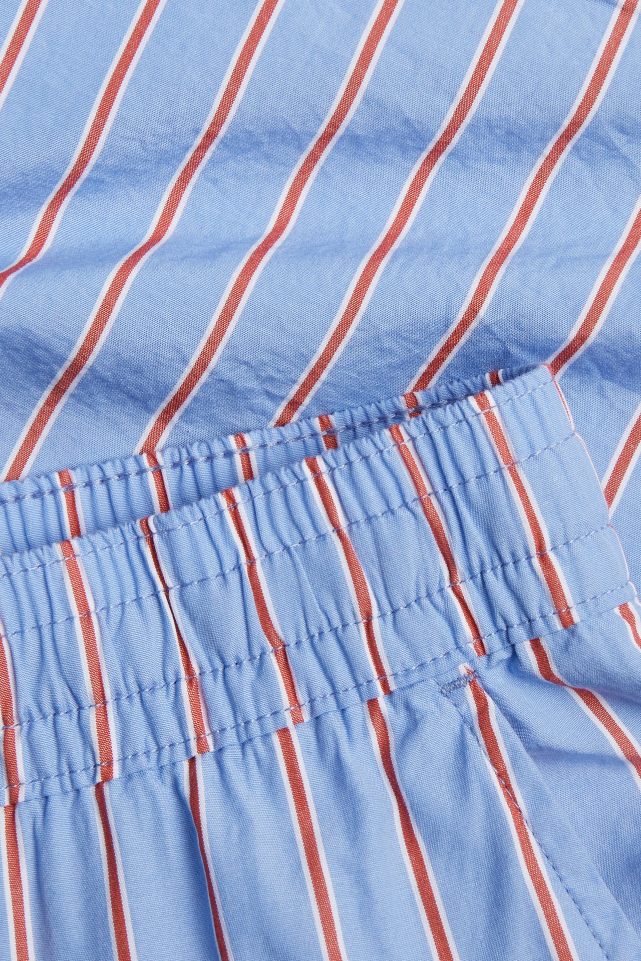 Nærbilde av blå bomullspoplinshorts for herre med røde og hvite striper og elastisk linning.