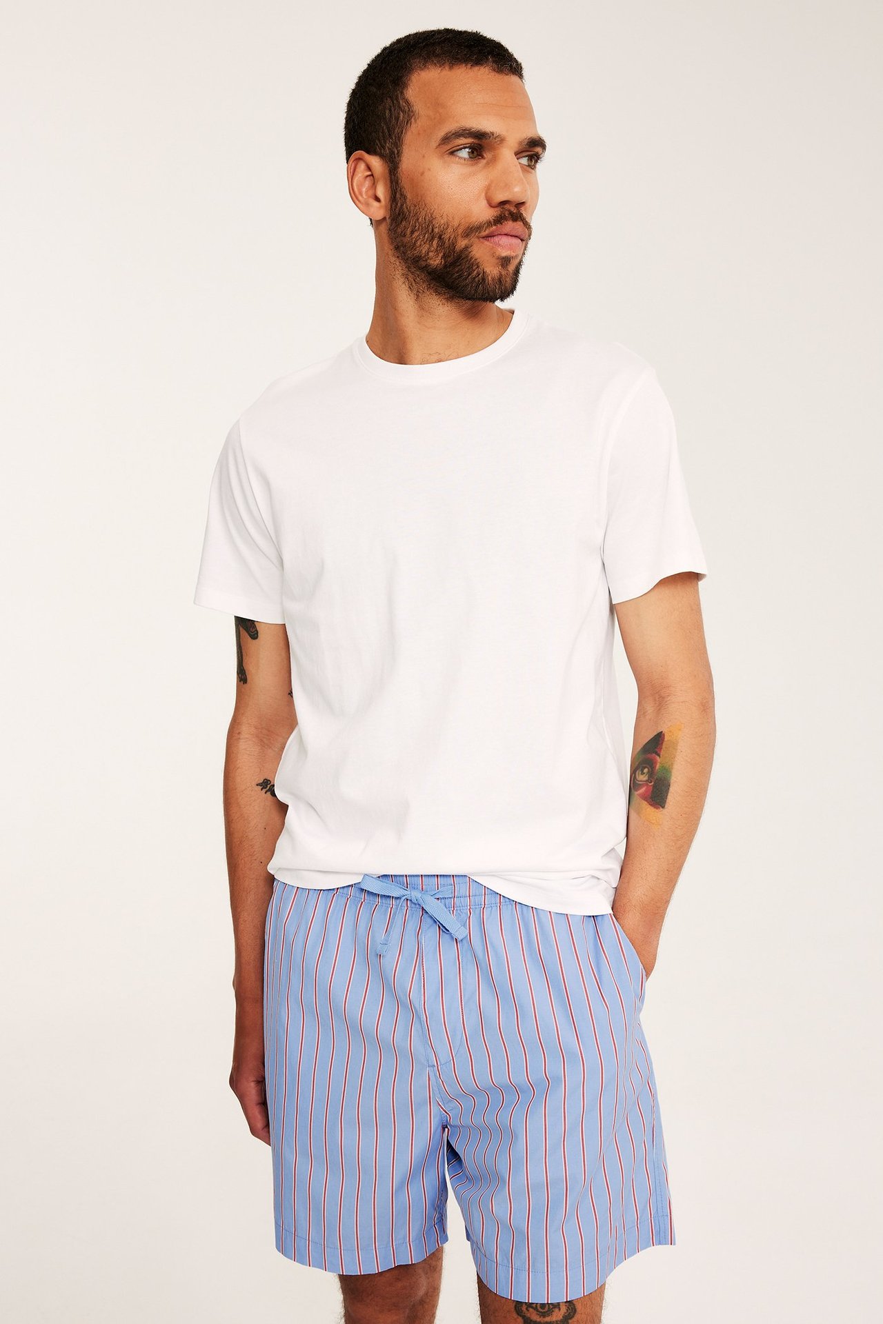 Framifrån, en man i blårandiga shorts av bomullspoplin med dragsko och en vit t-shirt.