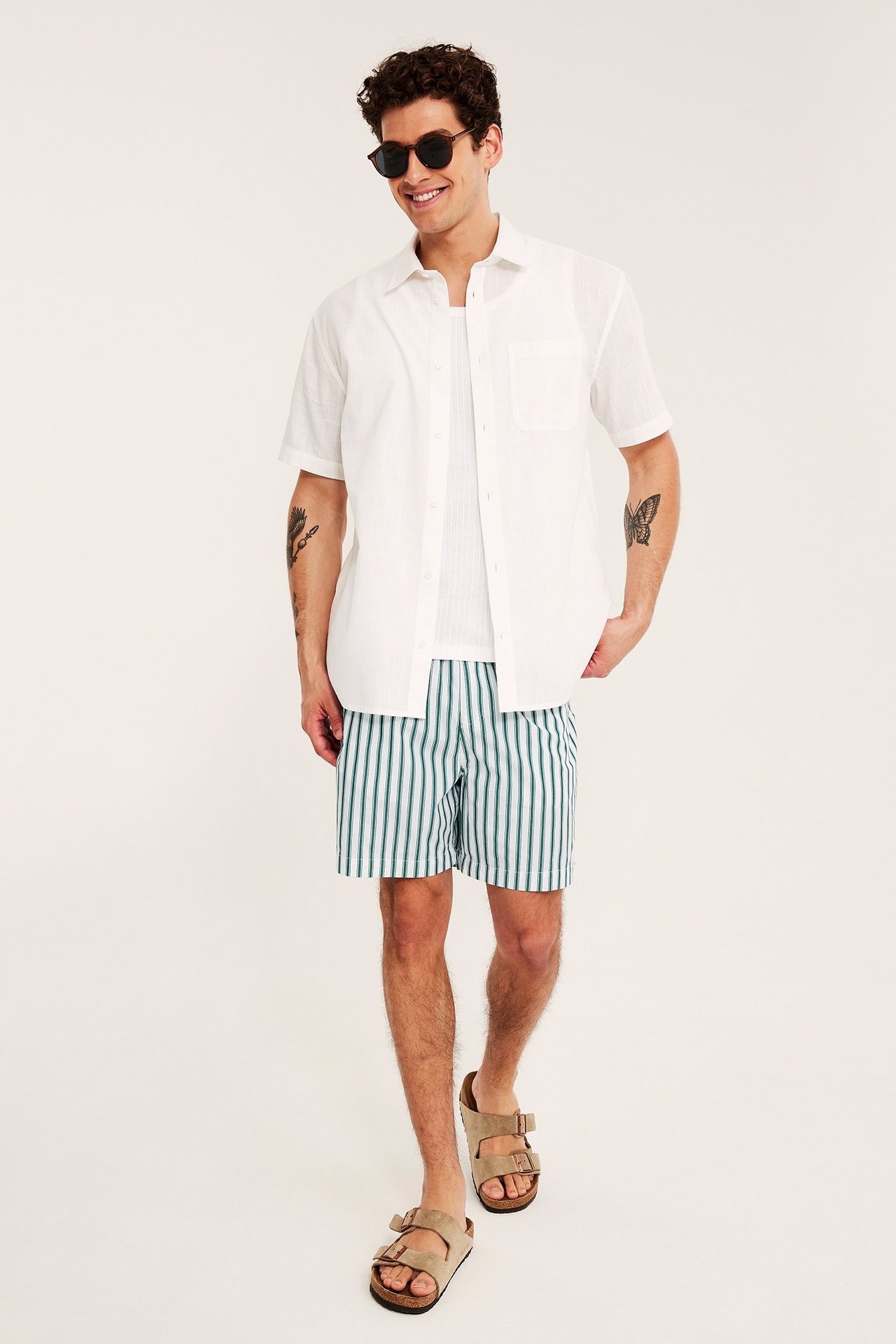 Framsida: Man i vit- och grönrandiga bomullsshorts, öppen vit skjorta, vitt linne, bruna sandaler.