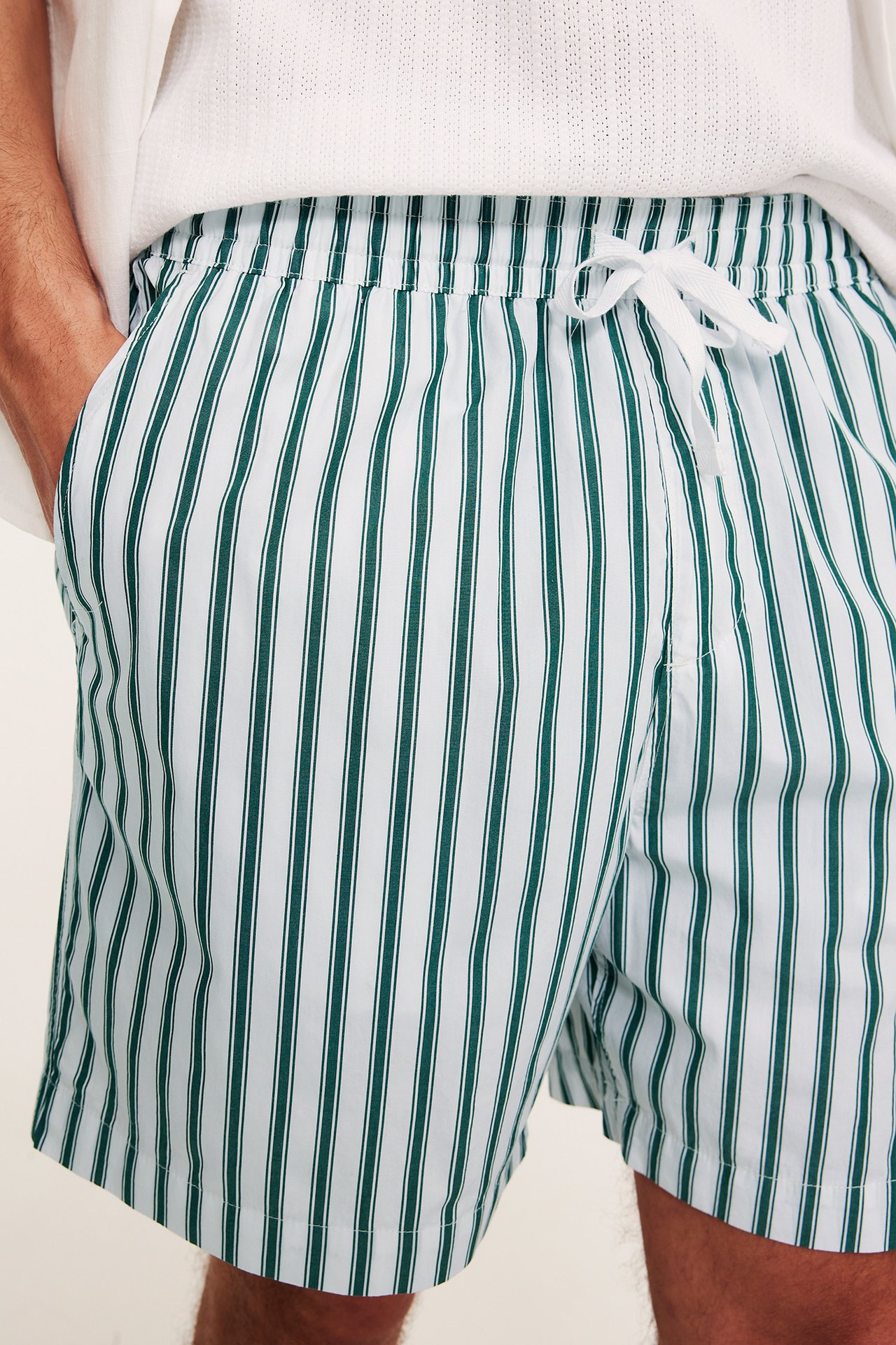Nærbilde forfra av en mann i avslappede hvite bomullspoplinshorts med grønne striper og hvit snøring.