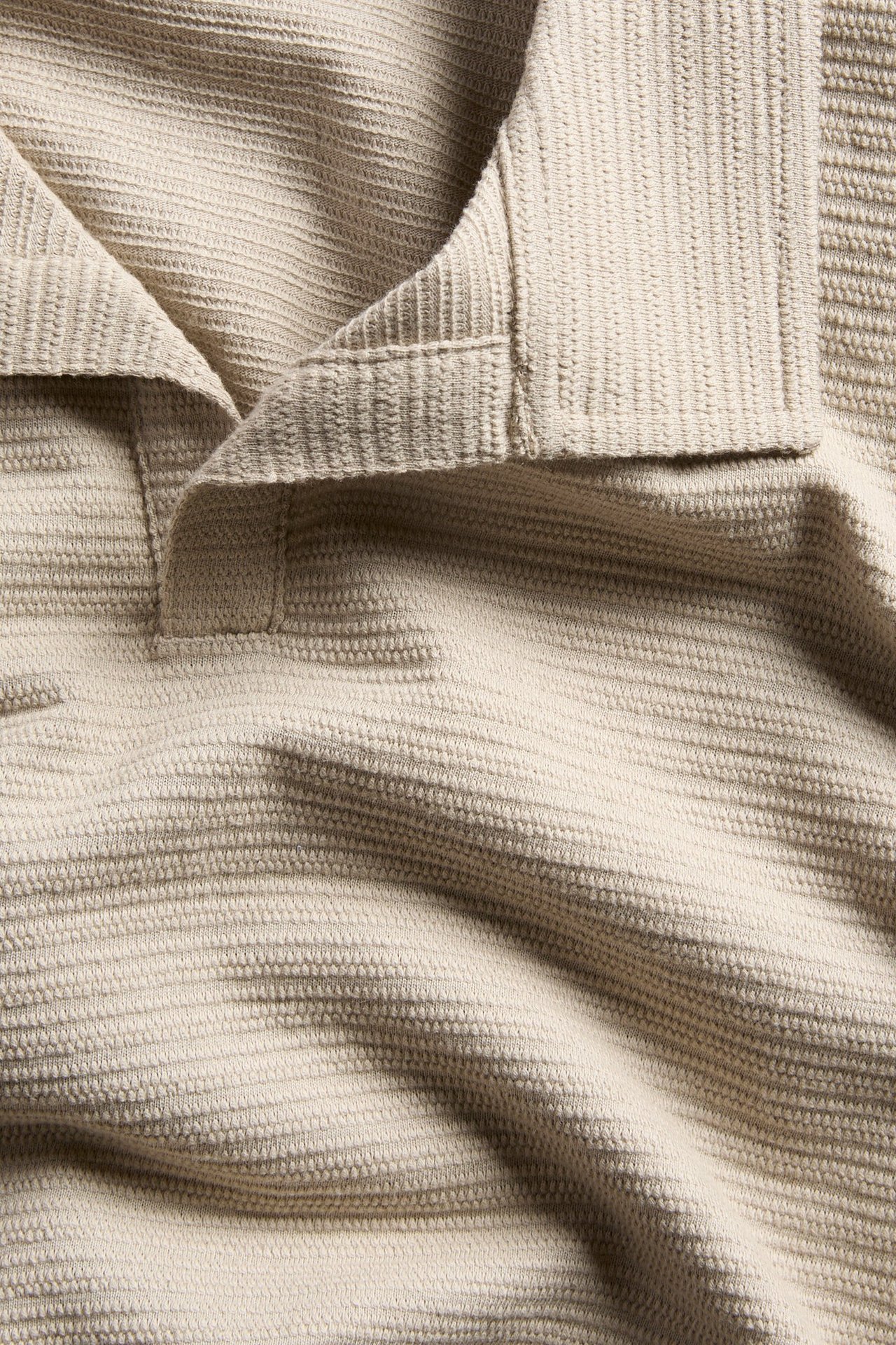 Närbild på en beige pikétröja i bomull med strukturtyg och klassisk krage.