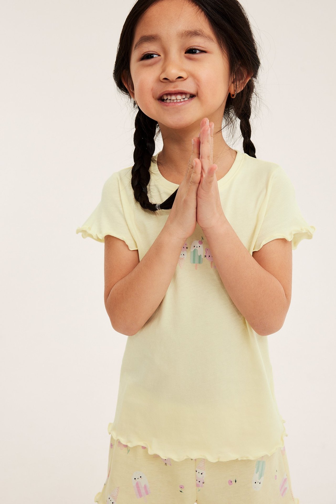 Widok z przodu: dziecko w jasnożółtej piżamie bawełnianej z krótkim rękawem, falbanami i nadrukiem lodów.
