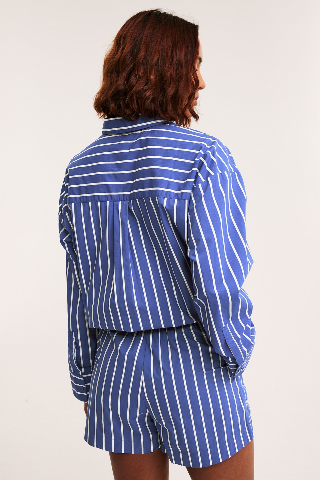 Naisen selkä, yllään sinivalkoraidalliset puuvillashortsit ja yhteensopiva pitkähihainen paita.