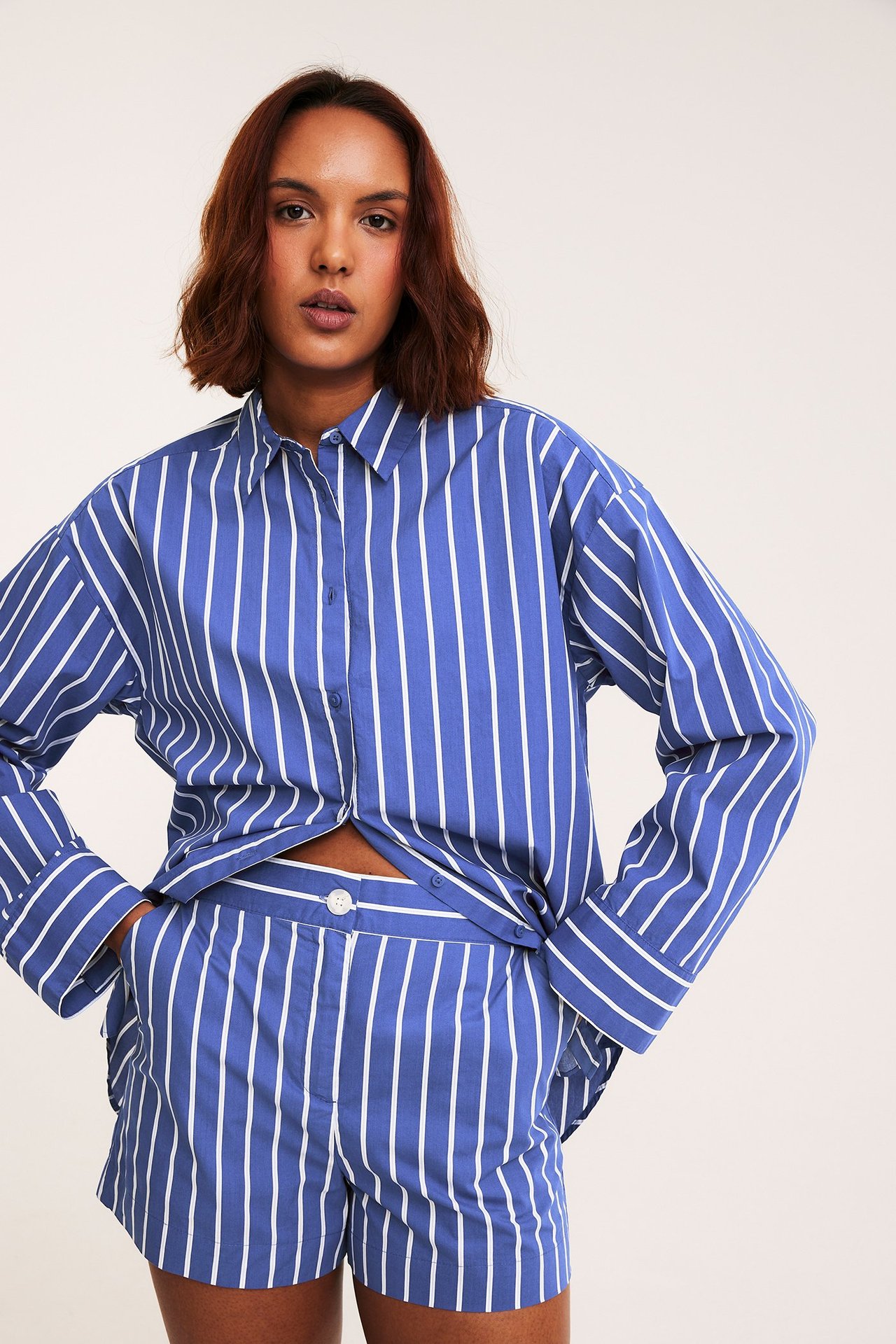 Edestäpäin kuvattu nainen sinivalkoraidallisissa puuvillapopliinishortseissa ja yhteensopivassa paidassa.