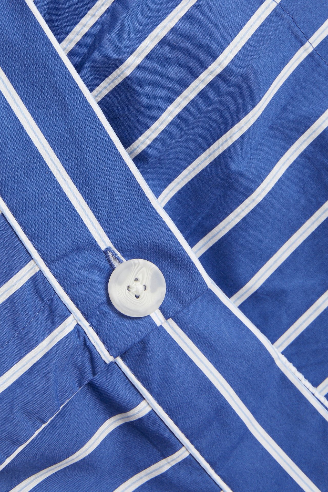 Zbliżenie na niebiesko-białą tkaninę z popeliny bawełnianej w paski z białym guzikiem.