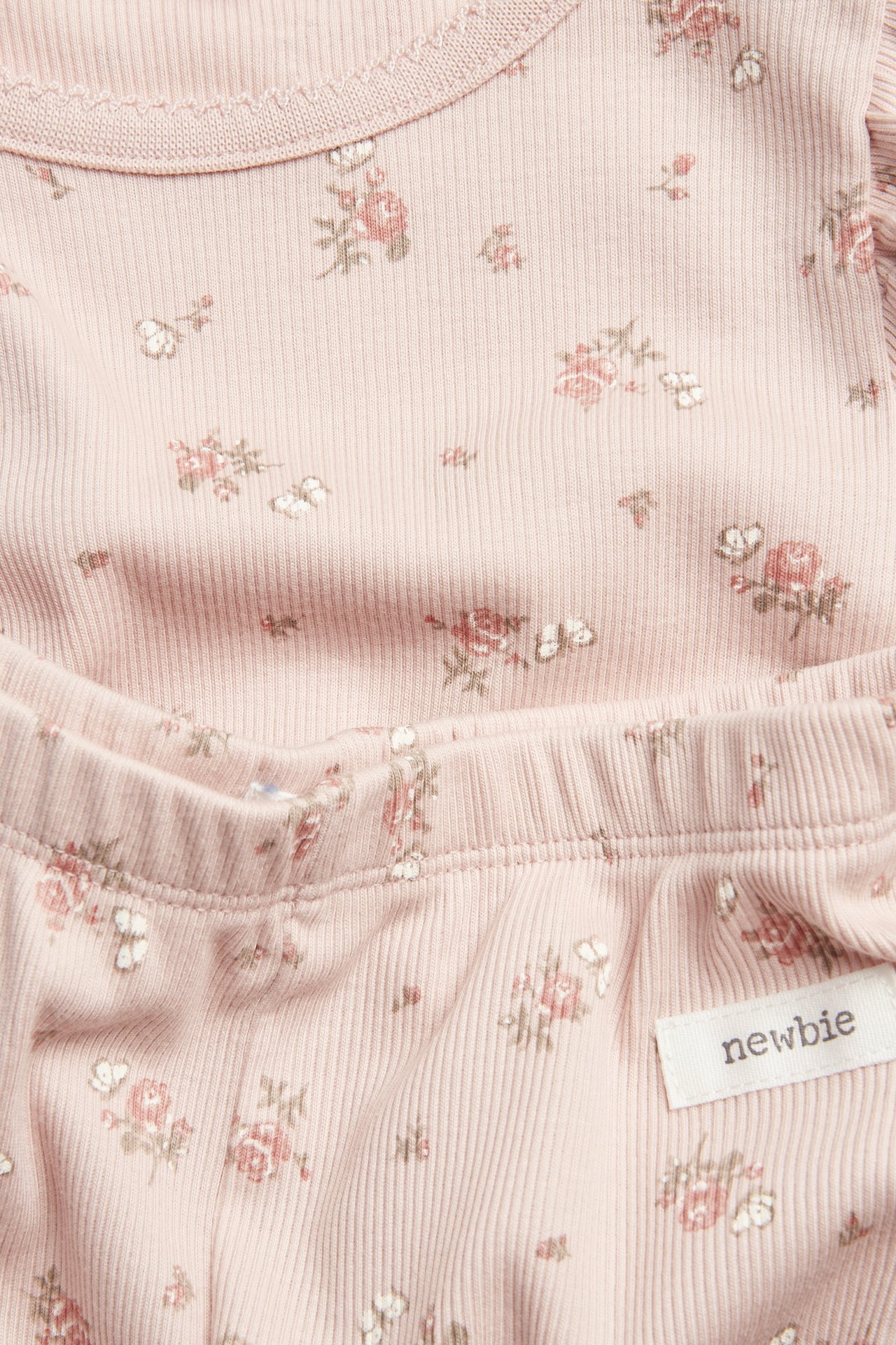 Nærbilde, forfra, av en rosa ribbestrikket todelt baby pyjamas i bomull med blomster- og sommerfuglmønster.