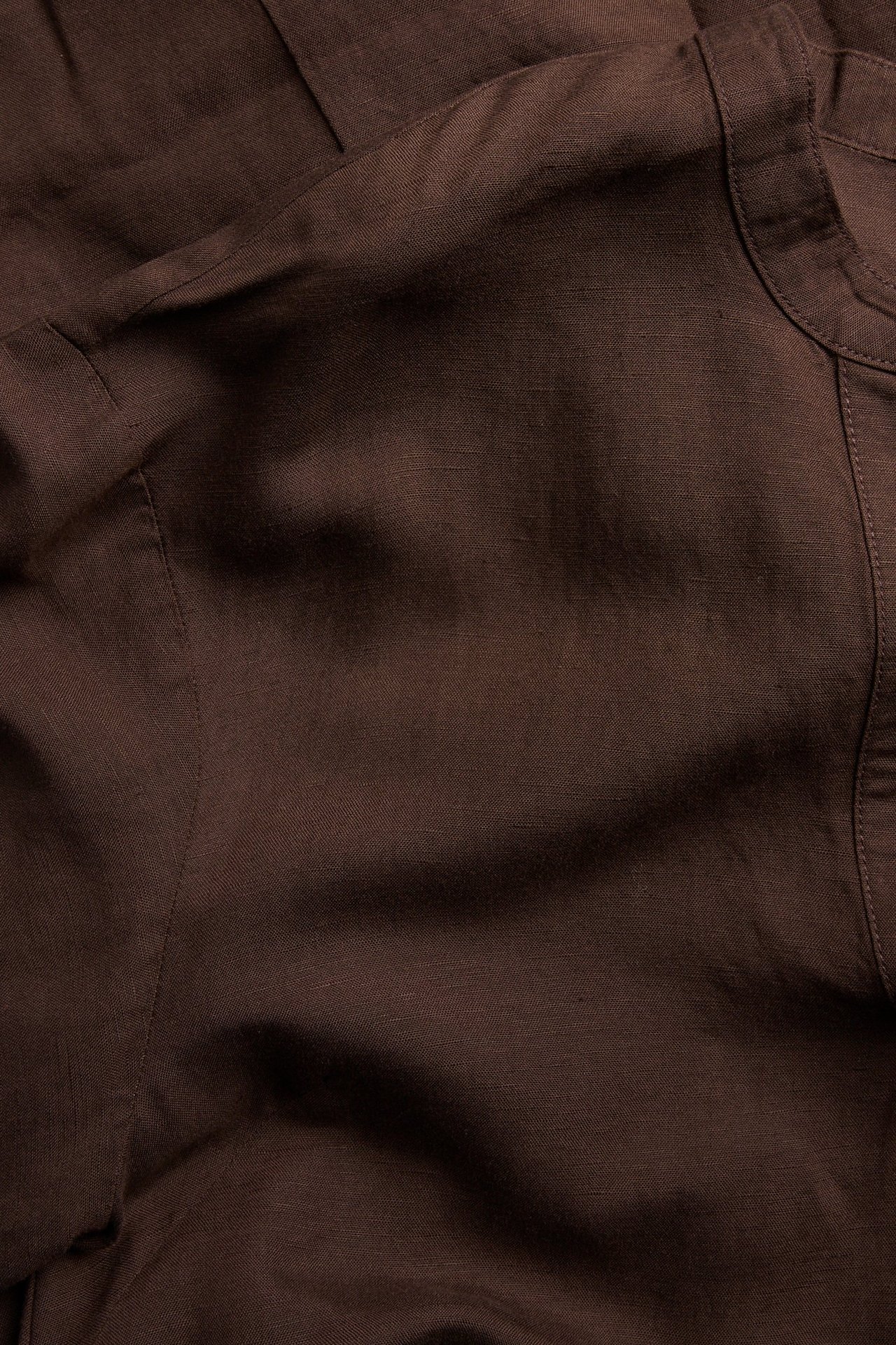 Närbild av en mörkbrun V-ringad klänning i linnemix, som visar tygets struktur och sömmar.