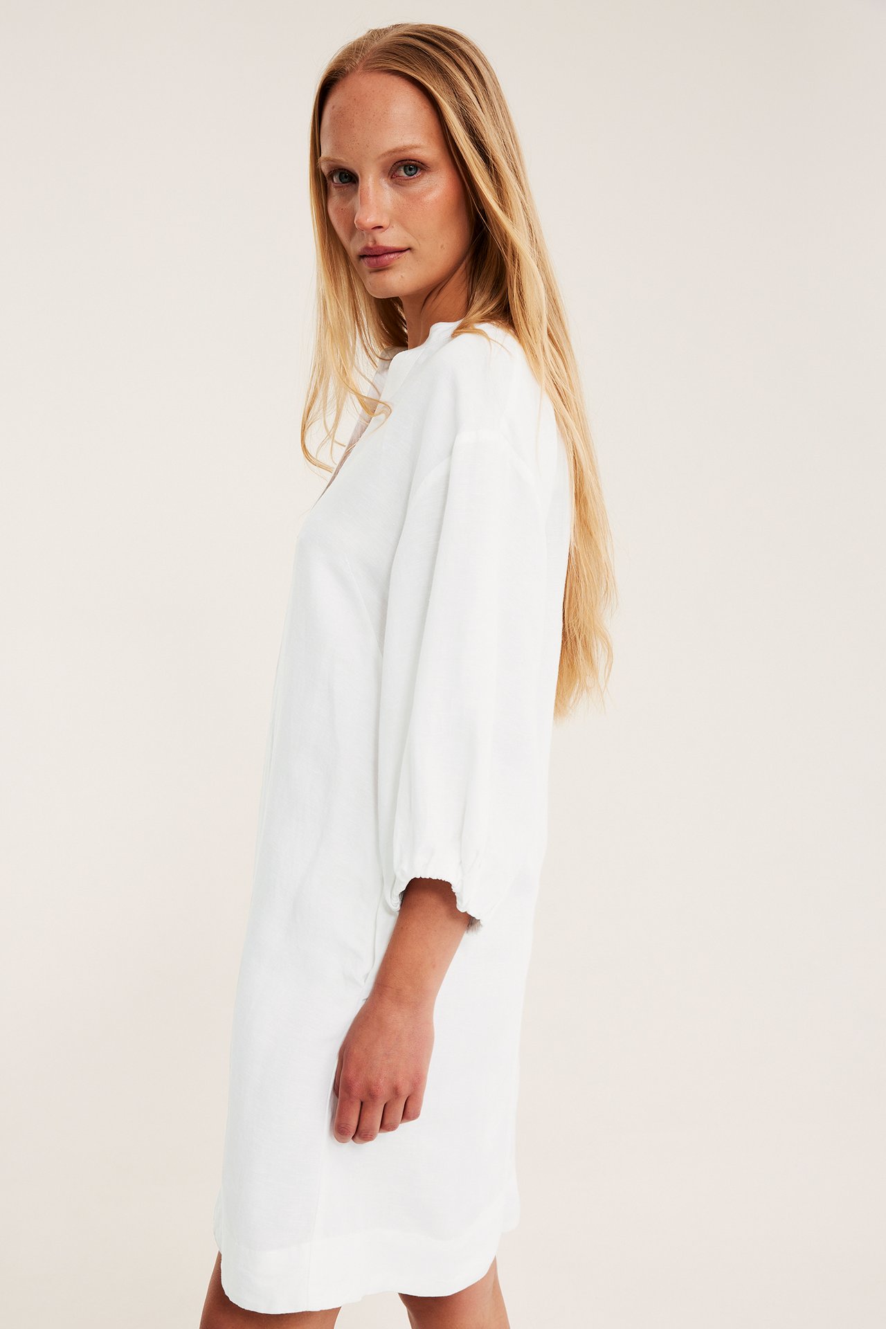 Sidovy av en kvinna i en vit V-ringad klänning i linnemix med ballongärmar.