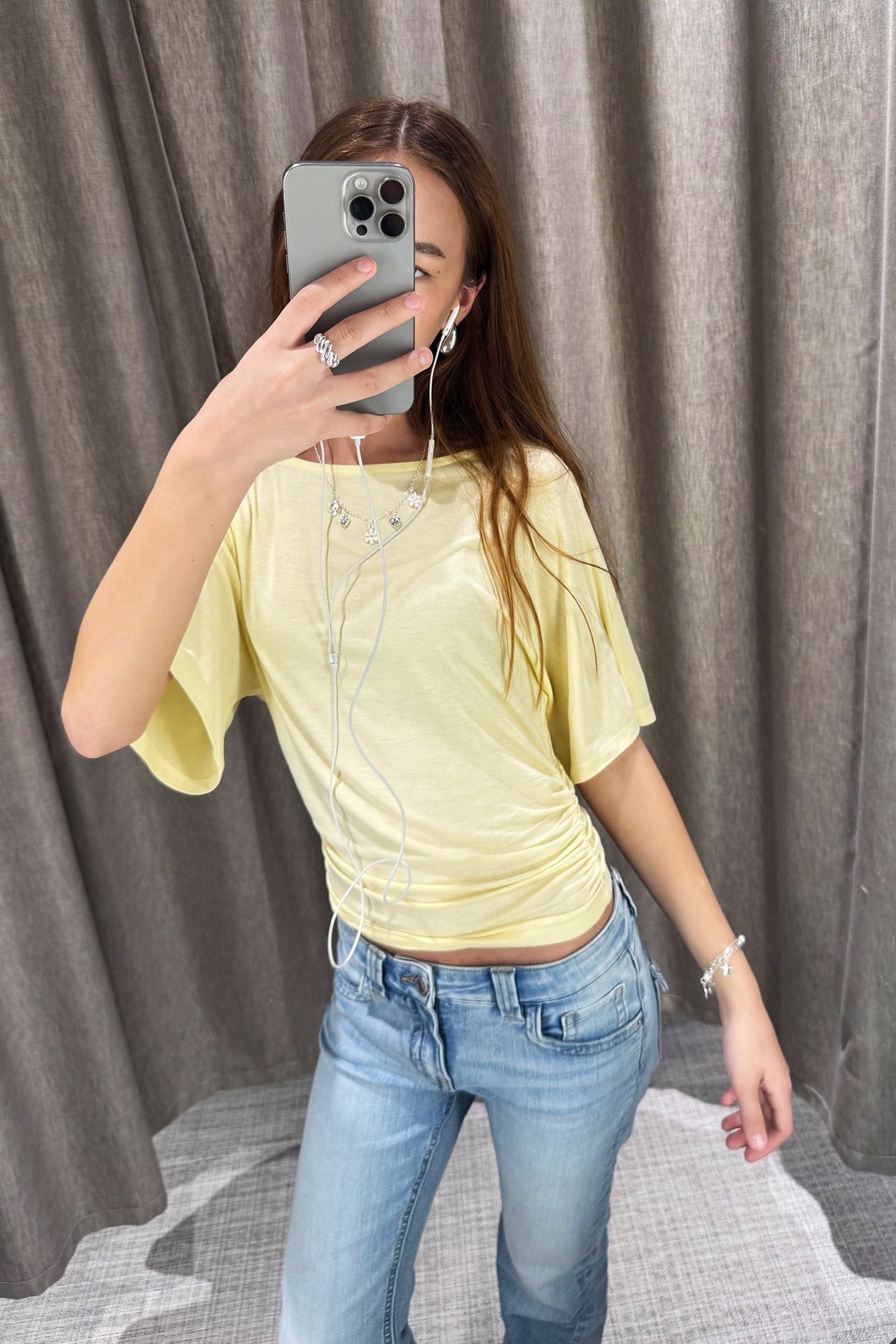 Framifrån: Kvinna i ljusgul draperad topp med fjärilsärmar, rynkad midja och ljusblå jeans.