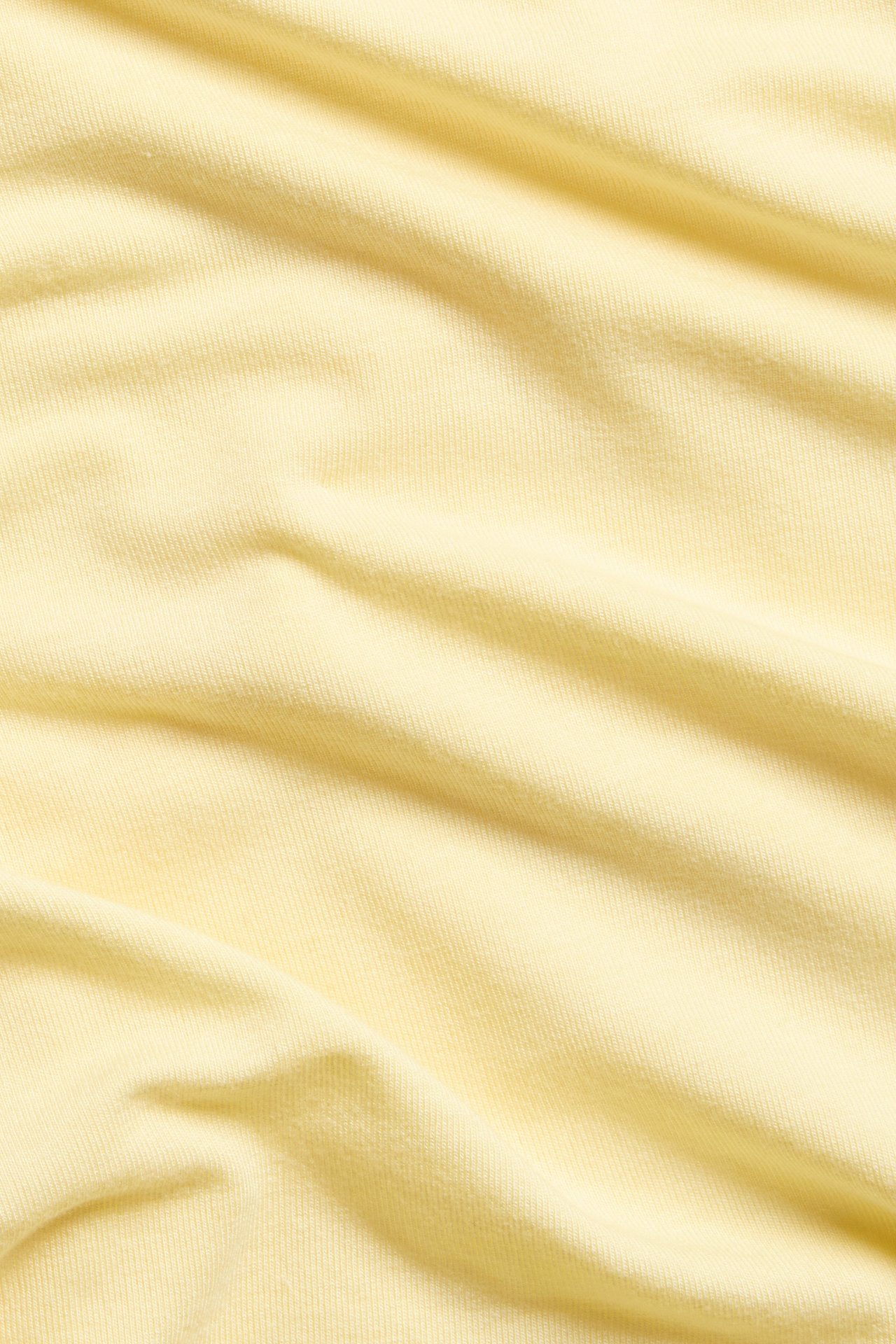Zbliżenie jasnego żółtego, drapowanego materiału topu, ukazujące miękkie fałdy i teksturę.