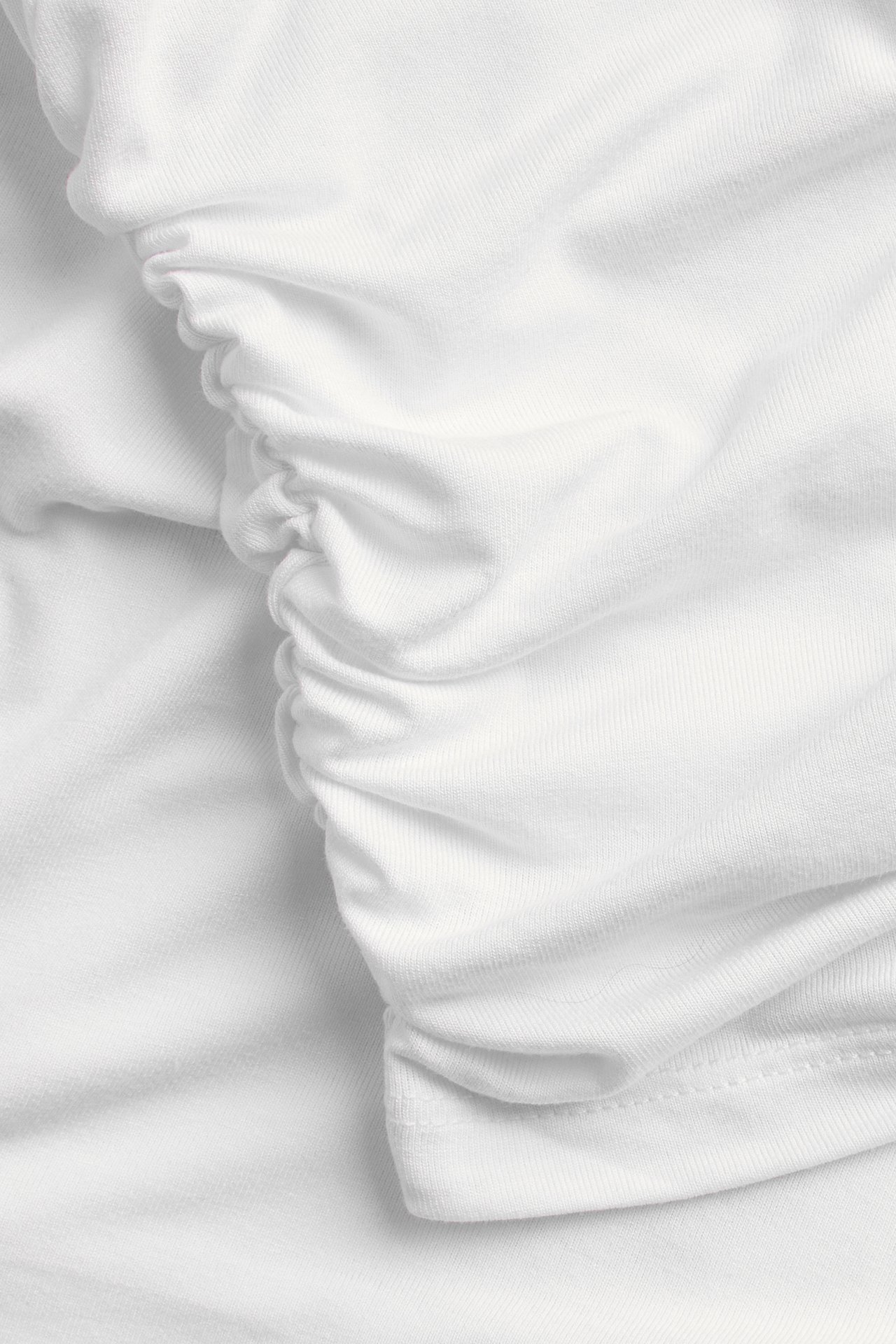 Närbild av en vit draperad topp med rynkade detaljer på mjukt tyg.