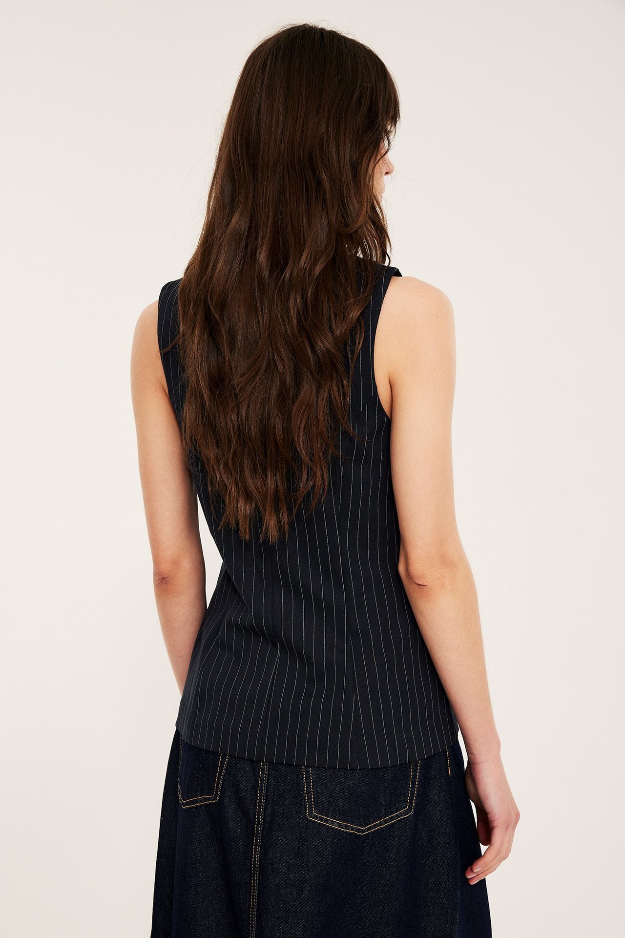 Ryggvy av kvinna i figursydd mörkblå kritstrecksrandig skräddad väst över mörkblå byxor.