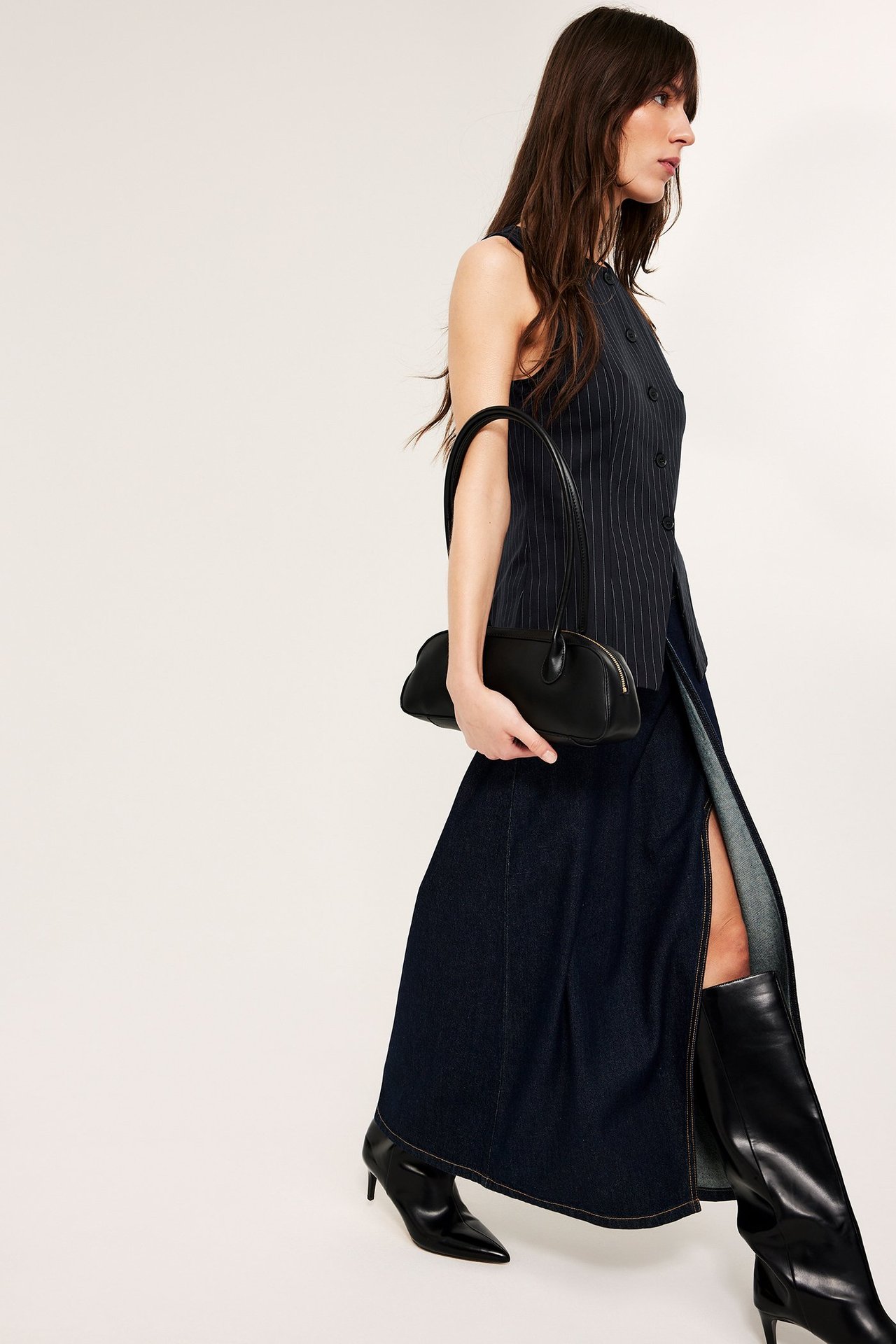 Side: Kvinne i mørkeblå stripete vest, langt dongeriskjørt, svarte støvler, holder svart veske.