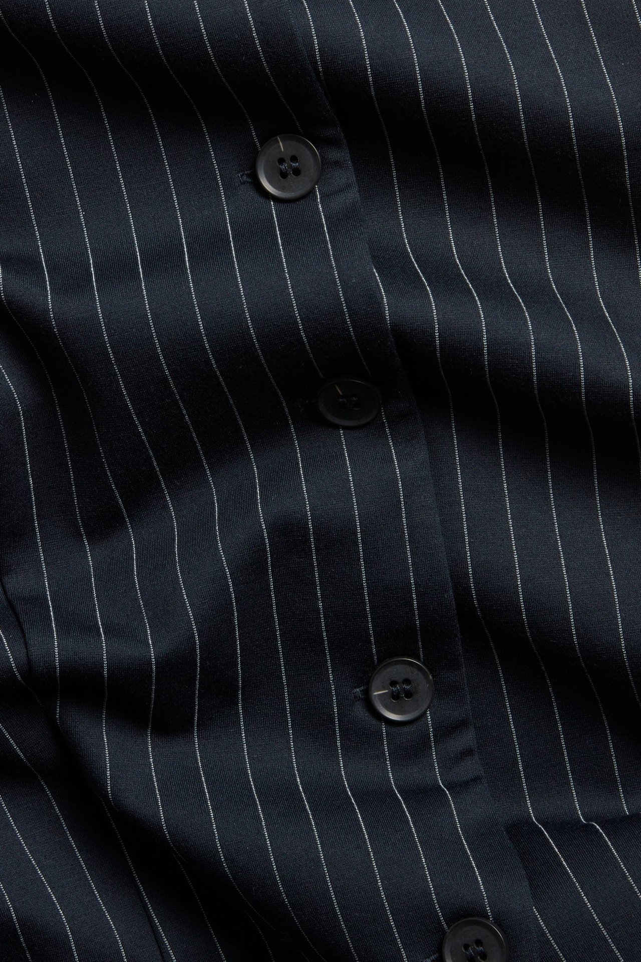 Zbliżenie na granatową kamizelkę w prążki o dopasowanym fasonie z ciemnymi guzikami.