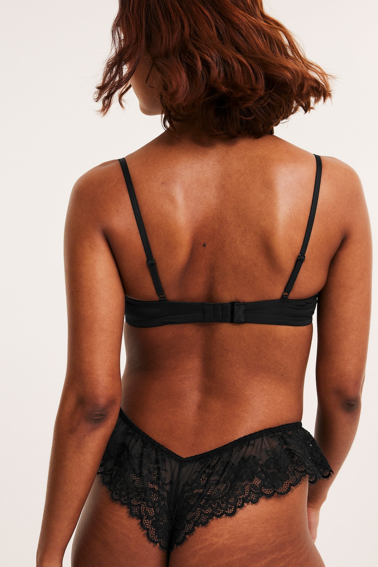 Widok z tyłu kobiety w czarnym koronkowym biustonoszu balconette z zapięciem i pasujących czarnych koronkowych majtkach.