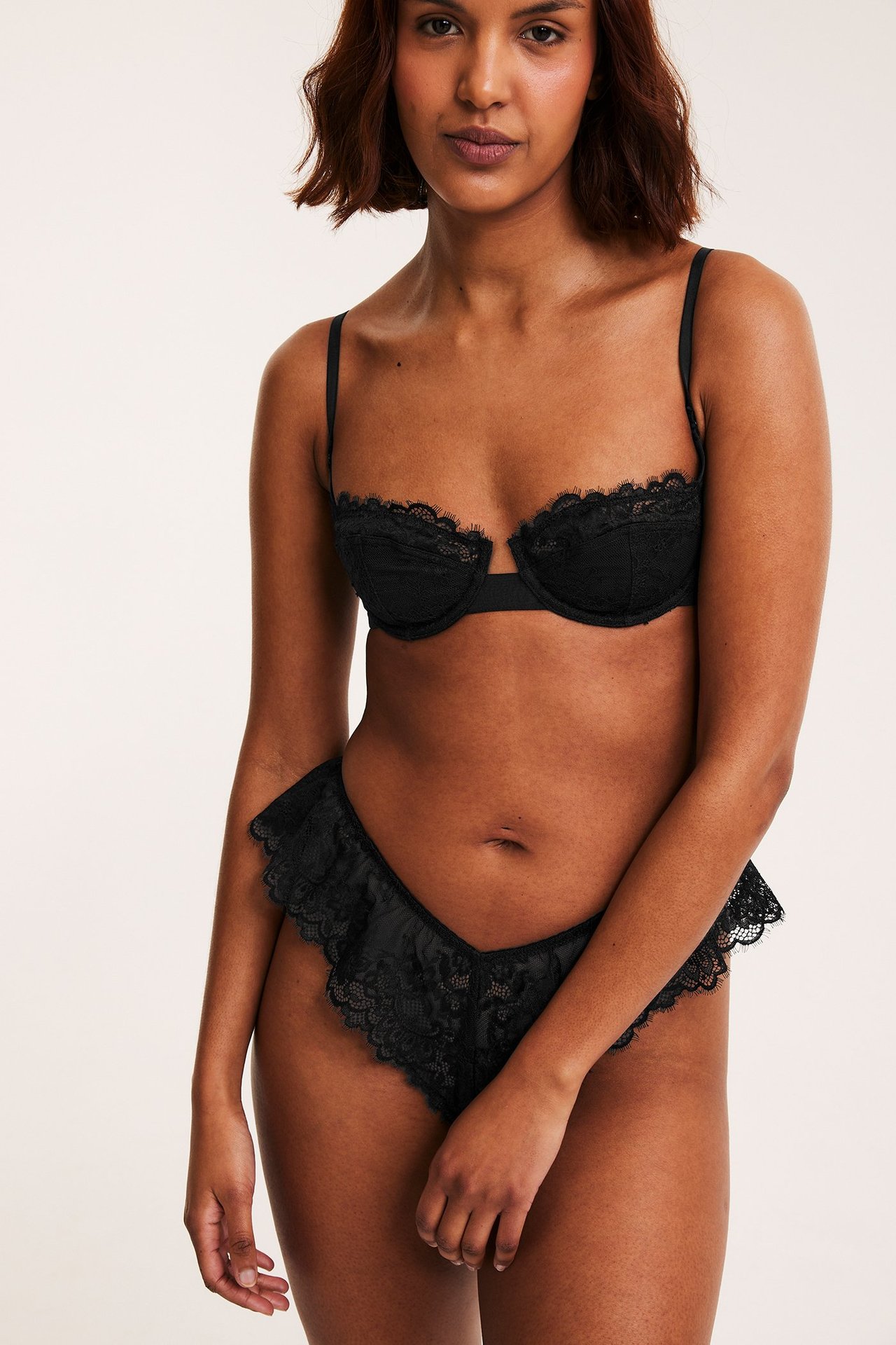Frontvy av en kvinna i en svart spetsbalconette-bh och matchande volangtrosor.