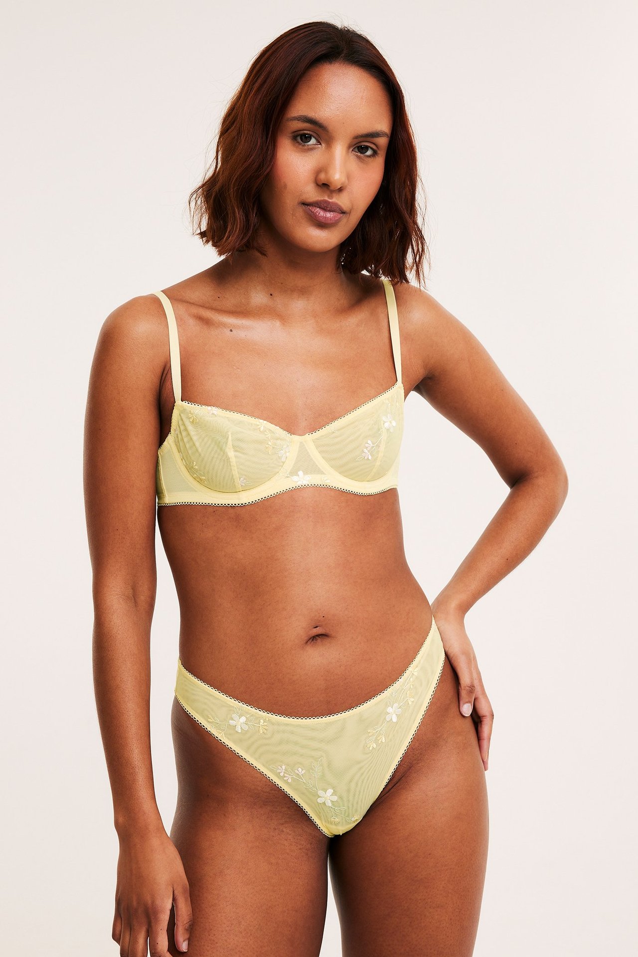 Frontutsikt av kvinne i lys gul mesh brazilian truse med hvite broderier og matchende BH.