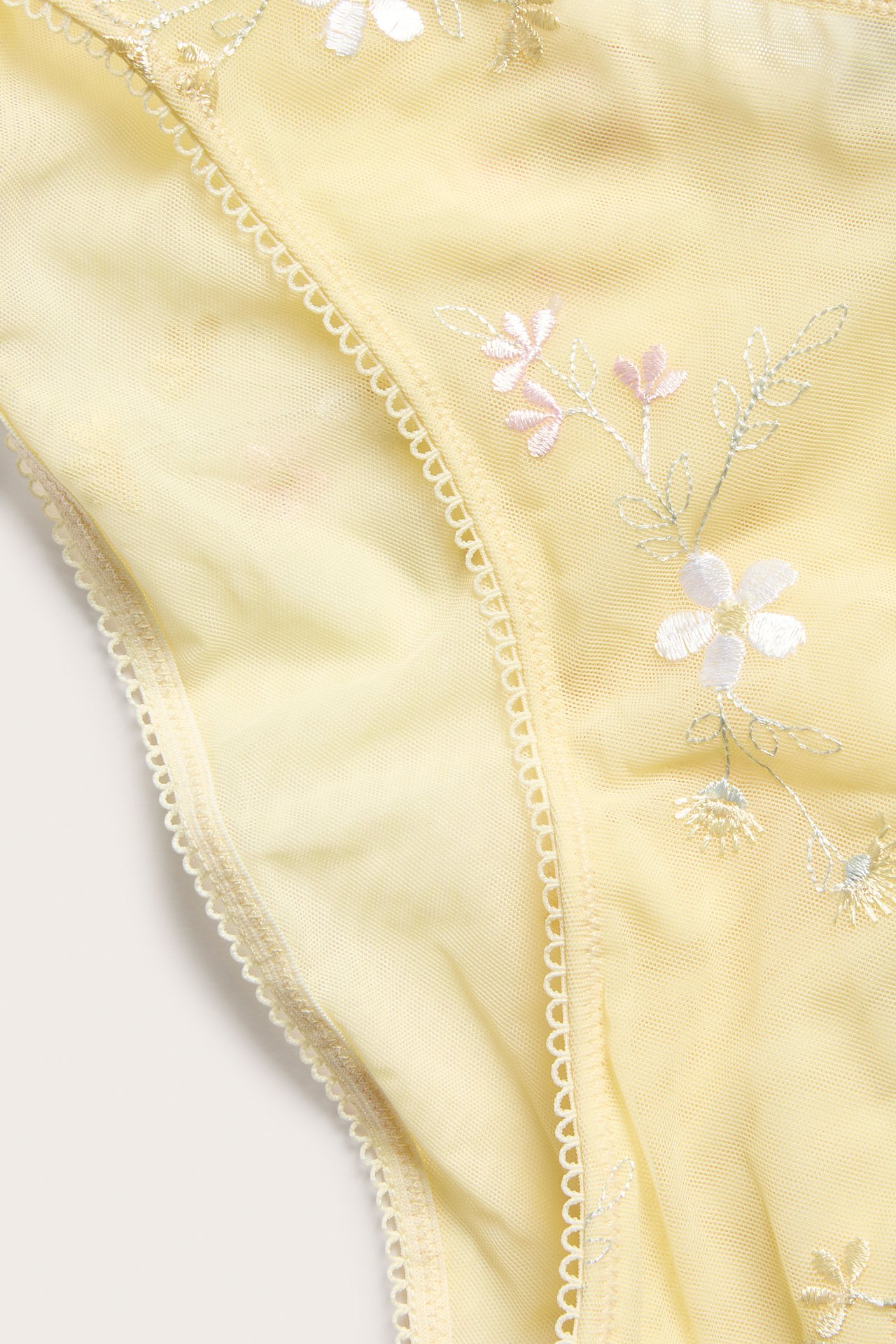 Zbliżenie na jasnożółte, prześwitujące figi brazylijskie z delikatnym białym i różowym haftem kwiatowym i gumką picot.