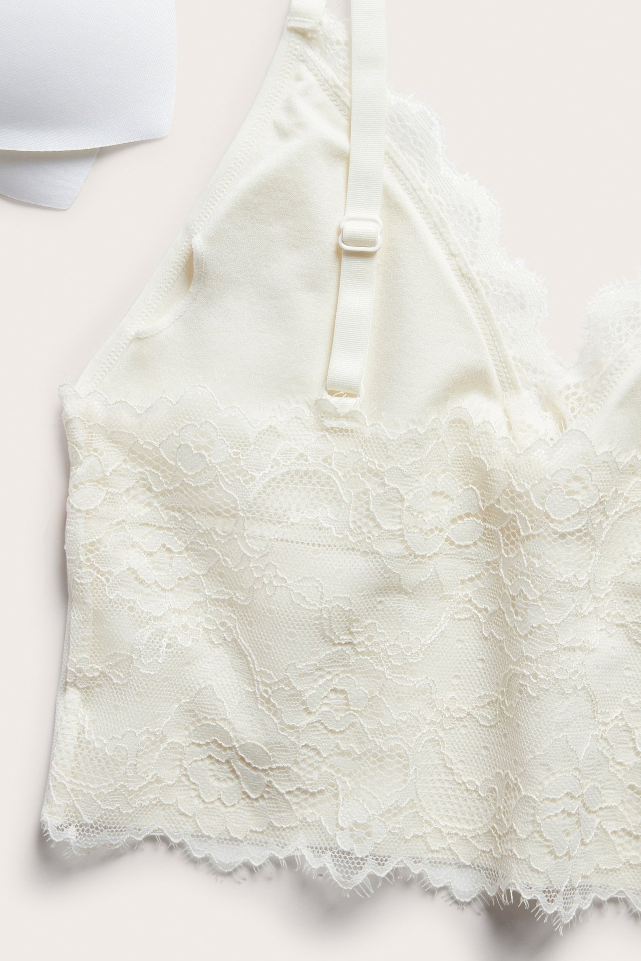 Nærbilde av offwhite bøyleløs BH med blondedetaljer og justerbar stropp, ved hvit BH-skål.