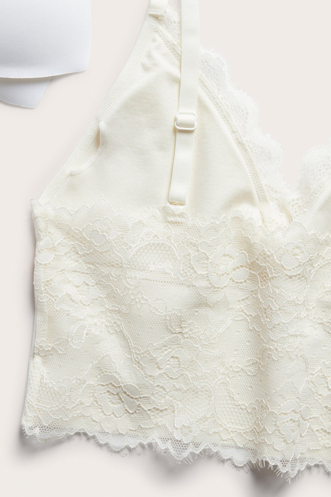 Zbliżenie na biustonosz bez fiszbin w kolorze ecru, z koronką i ramiączkiem, obok białej miseczki.