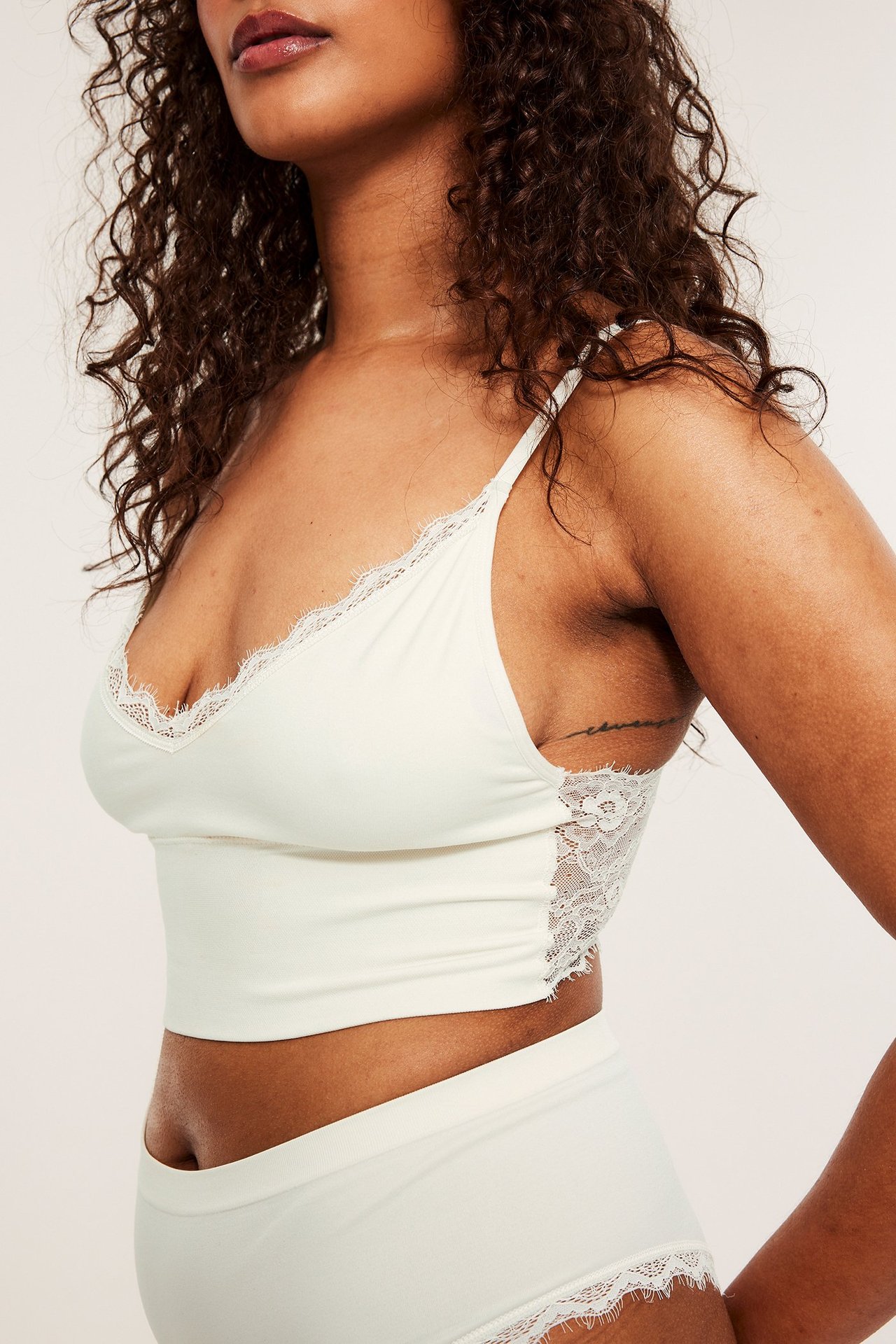 Sidebilde av en kvinne i en offwhite bøyleløs BH med blonder og matchende truse.