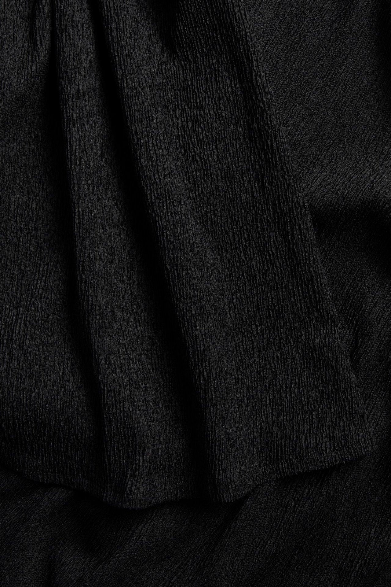 Zbliżenie czarnego topu imprezowego, ukazujące jego pogniecioną teksturę z poliestru.