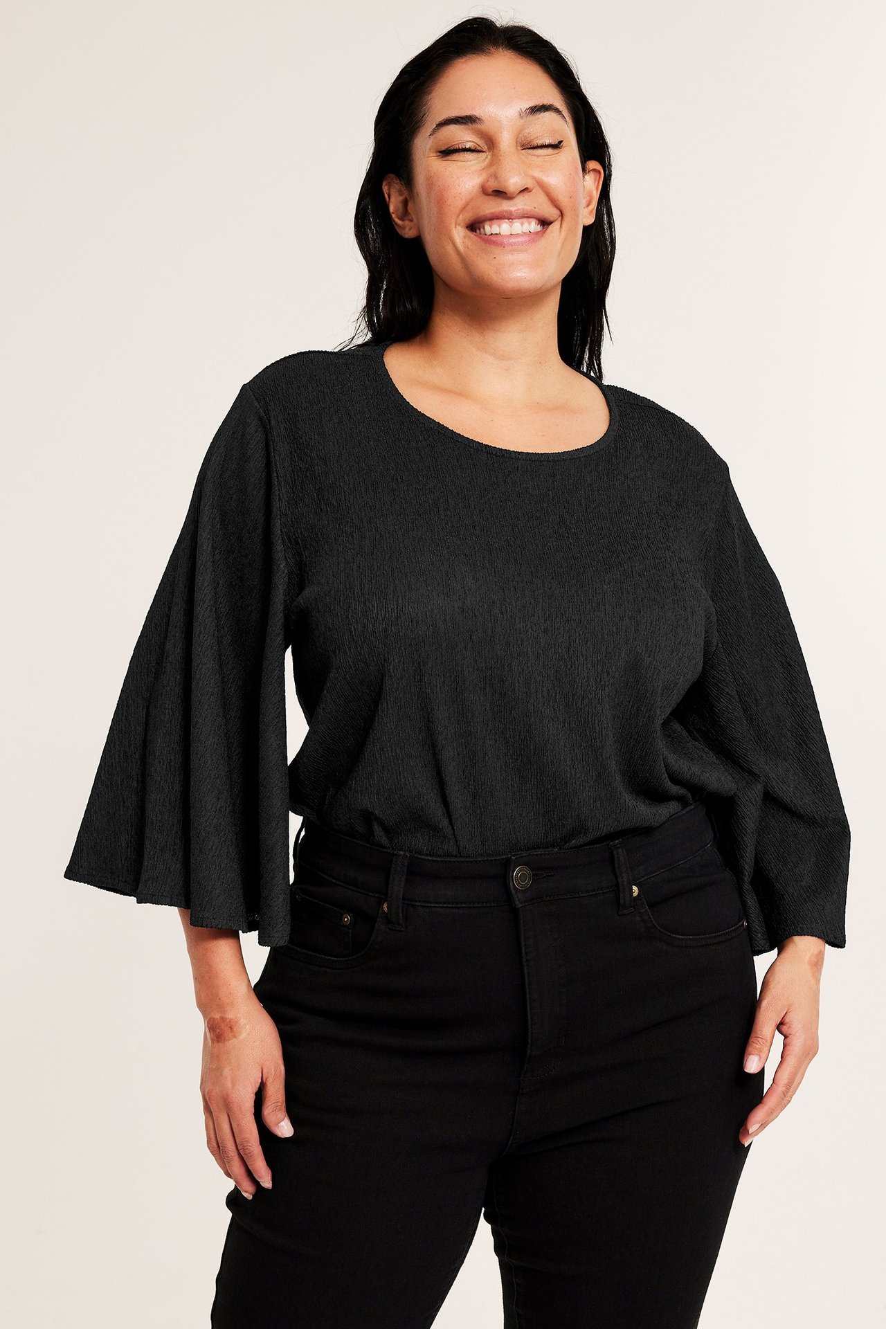 Z przodu: Kobieta w czarnym topie z długimi rękawami motylkowymi i czarnych dżinsach.