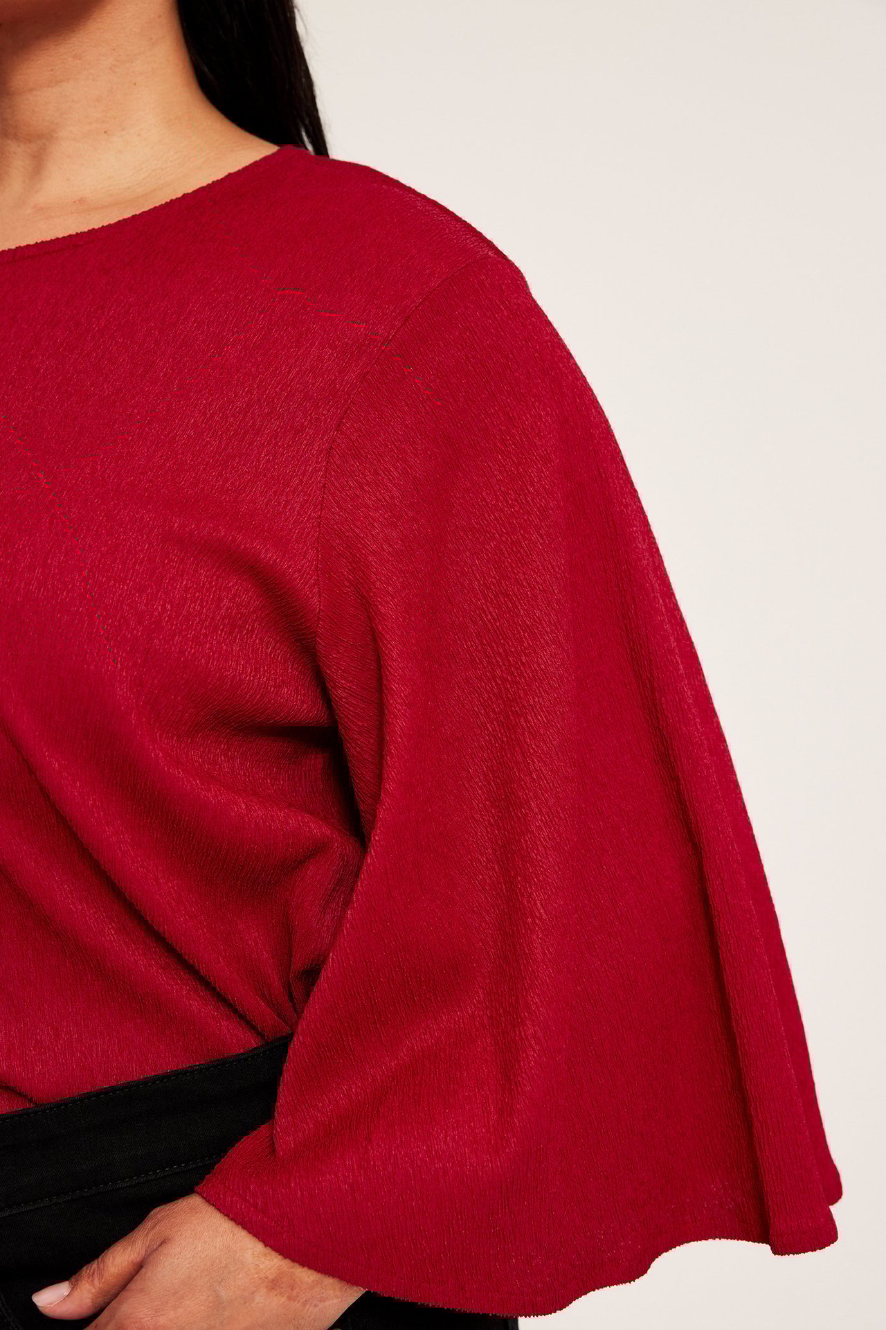 Närbild på en kvinna i röd texturerad festtopp med långa fjärilsärmar och svarta byxor.