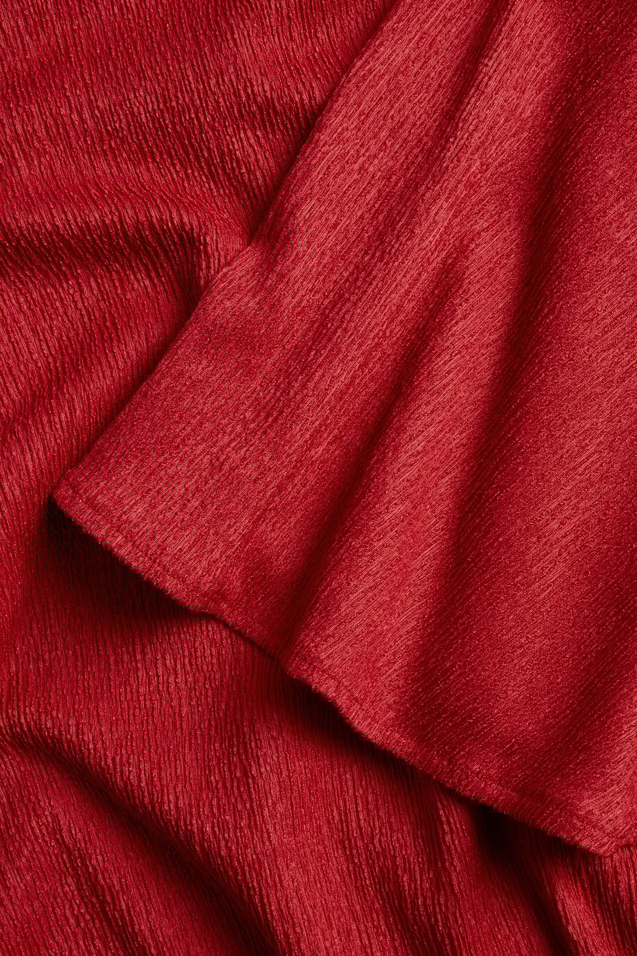 Zbliżenie czerwonej, teksturowanej tkaniny poliestrowej z topu imprezowego o marszczonej powierzchni.