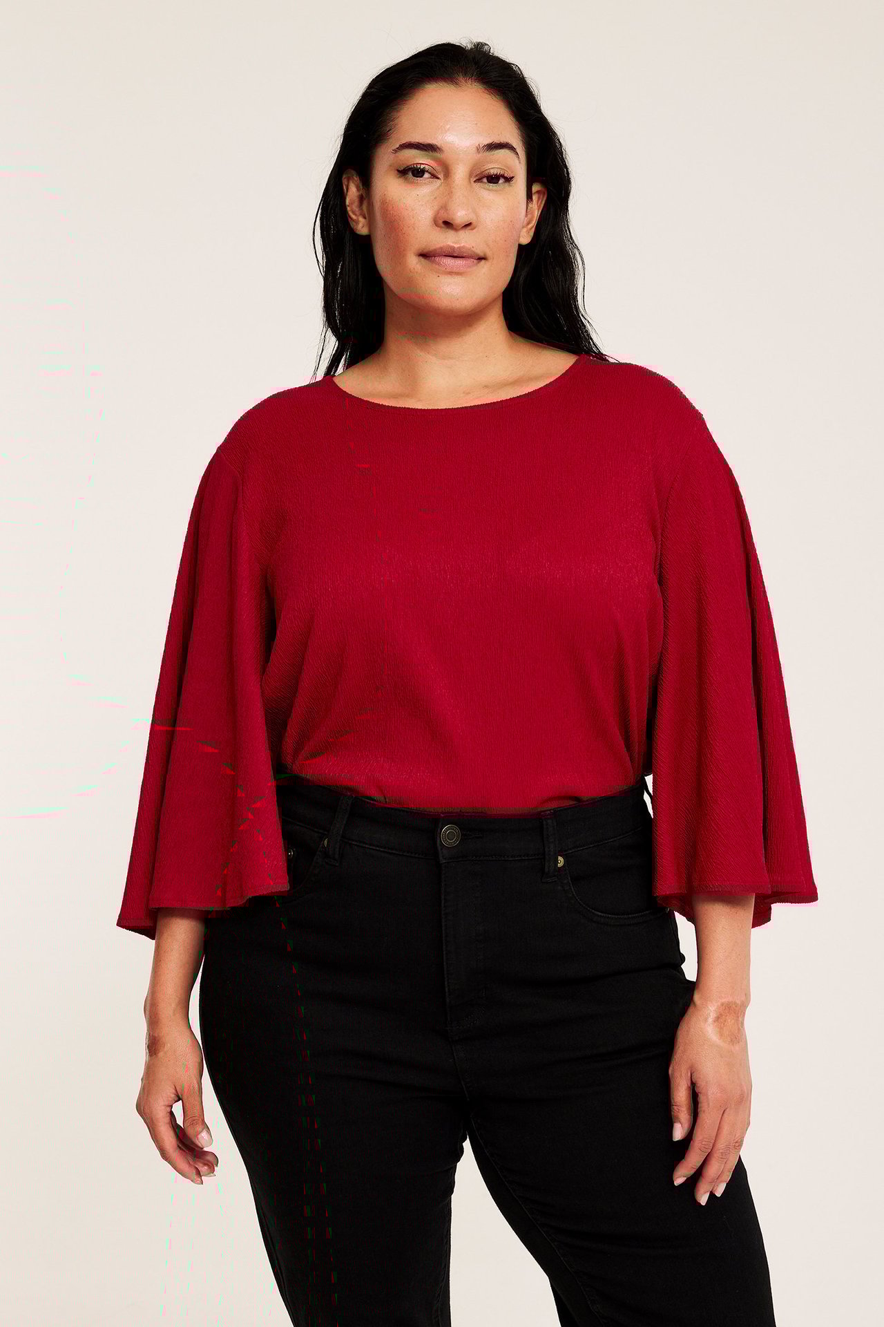 Widok z przodu kobiety w czerwonym topie imprezowym z długimi, szerokimi rękawami motylkowymi i czarnych dżinsach.