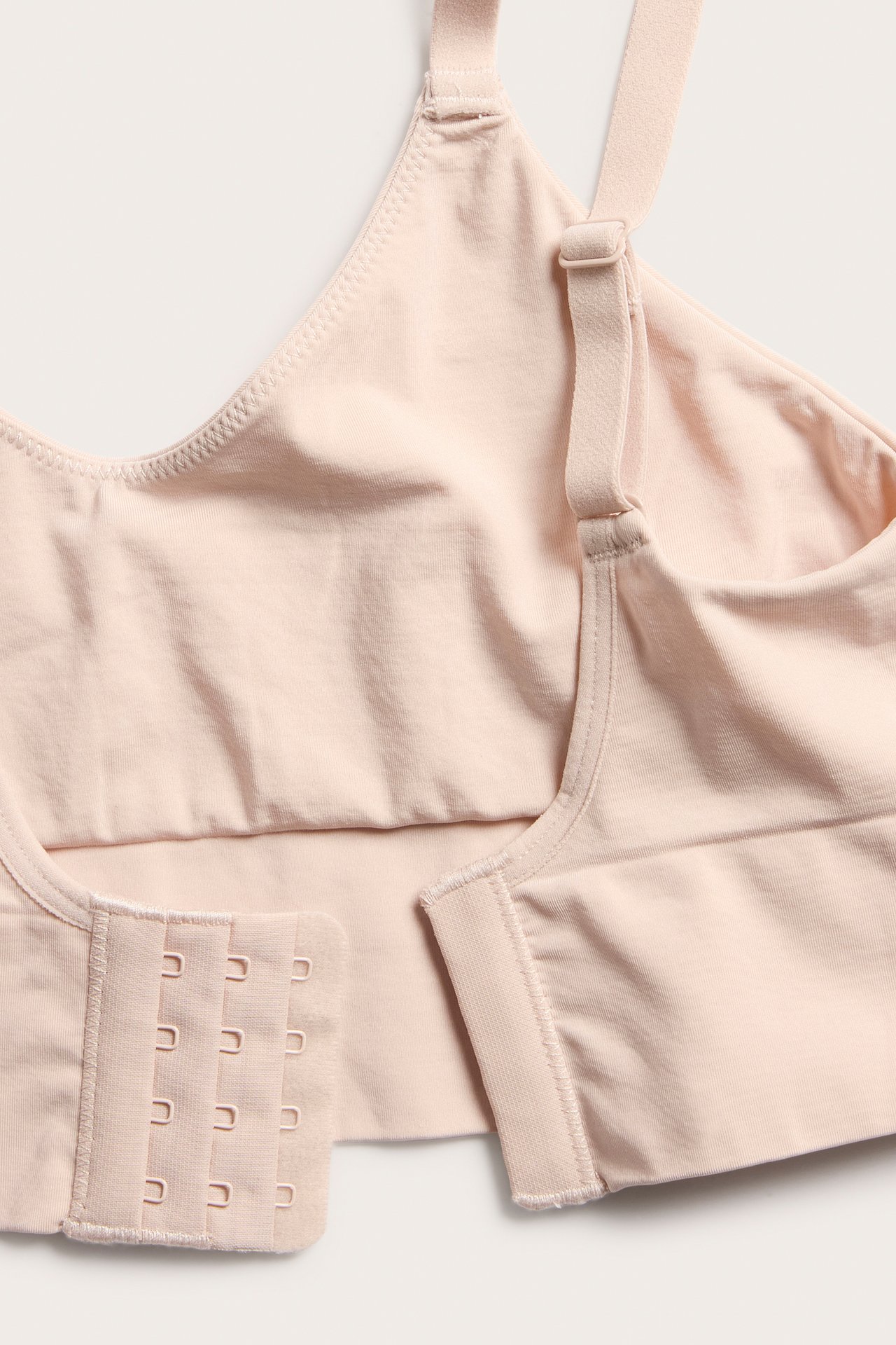 Lähikuva vaaleanpunaisista saumattomista rintaliiveistä säädettävillä olkaimilla ja hakaskiinnityksellä.