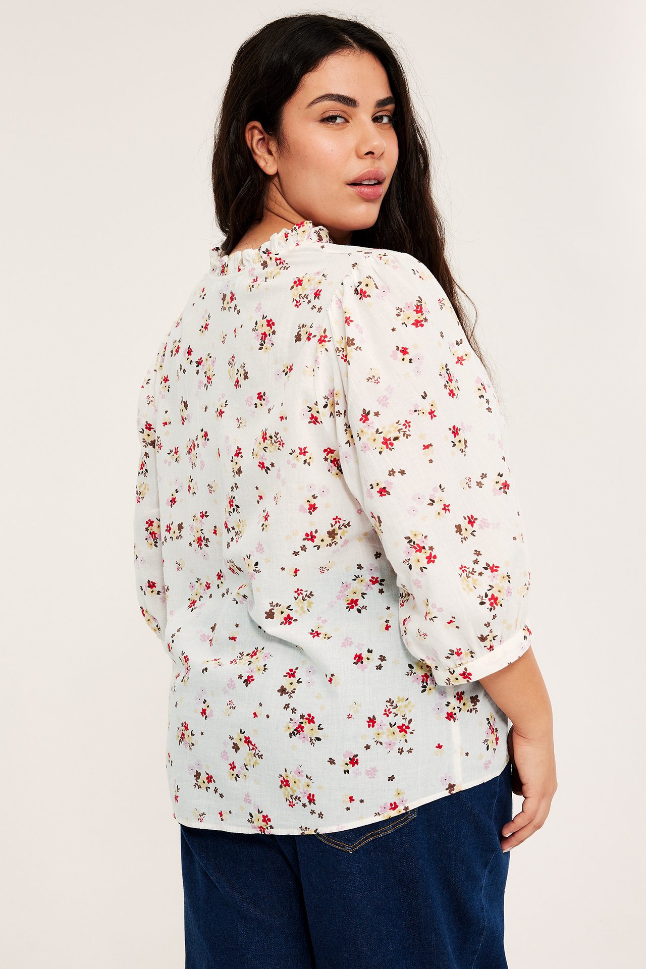 Nainen yllään luonnonvalkoinen kukkakuvioinen puuvillapusero, jossa röyhelökaulus ja puffihihat, taka-sivukuva.