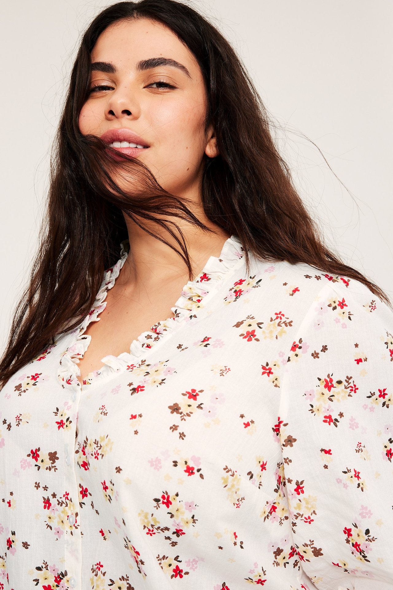 Zbliżenie na kobietę w białej bawełnianej bluzce we wzory kwiatowe z falbankowym dekoltem w serek.