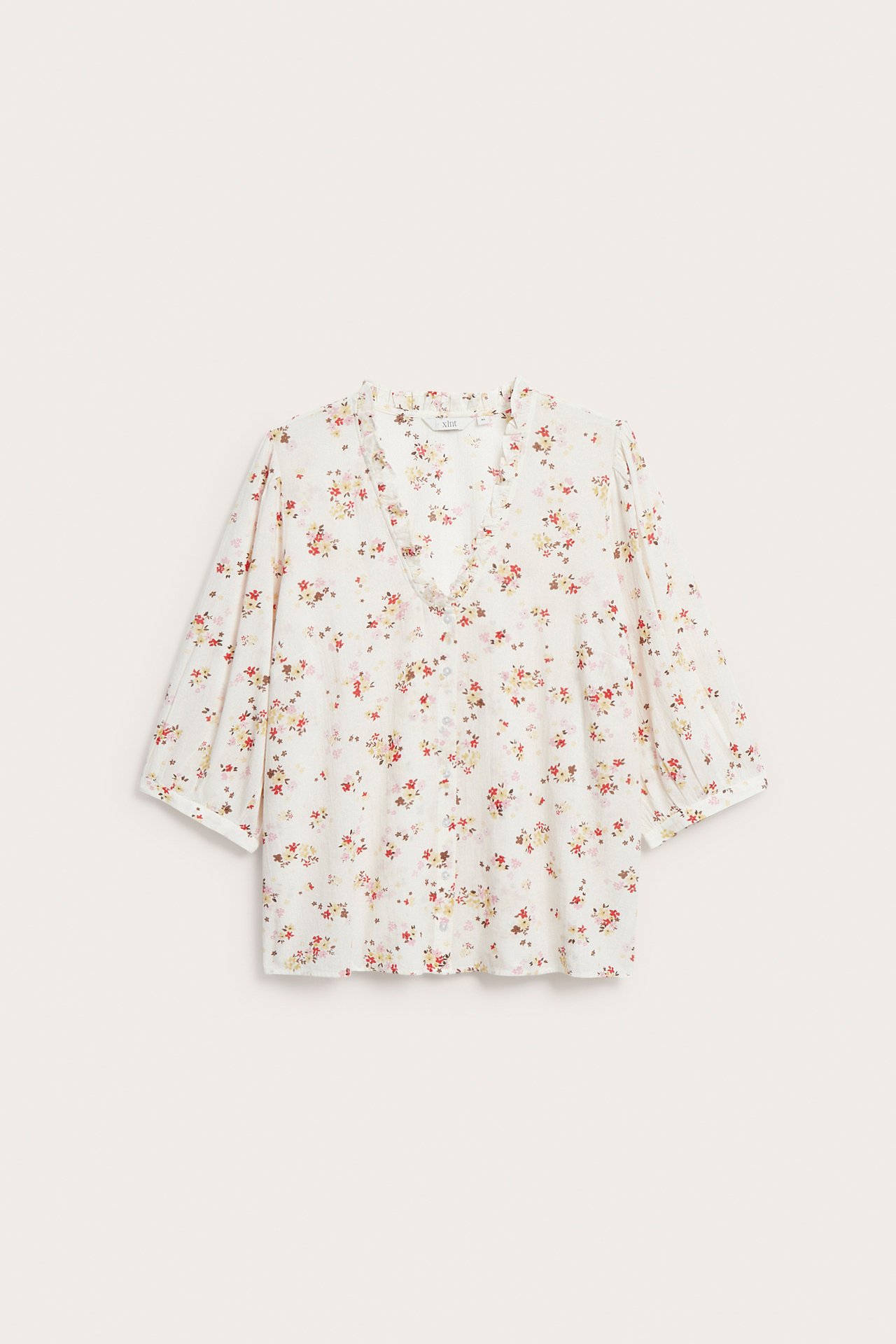 Edestä: luonnonvalkoinen puuvillapusero värikkäällä kukkakuviolla, röyhelö-V-pääntie ja 3/4-puhvihihat.