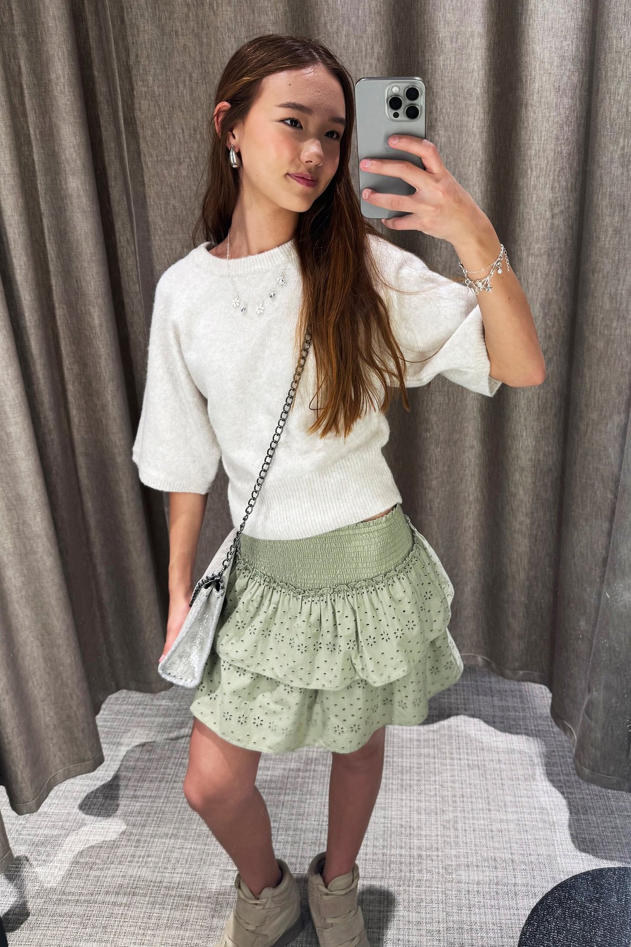 Widok z przodu: Dziecko nosi ciemnozieloną spódniczkę z haftem angielskim, marszczoną talią, jasny sweter, srebrną torebkę.