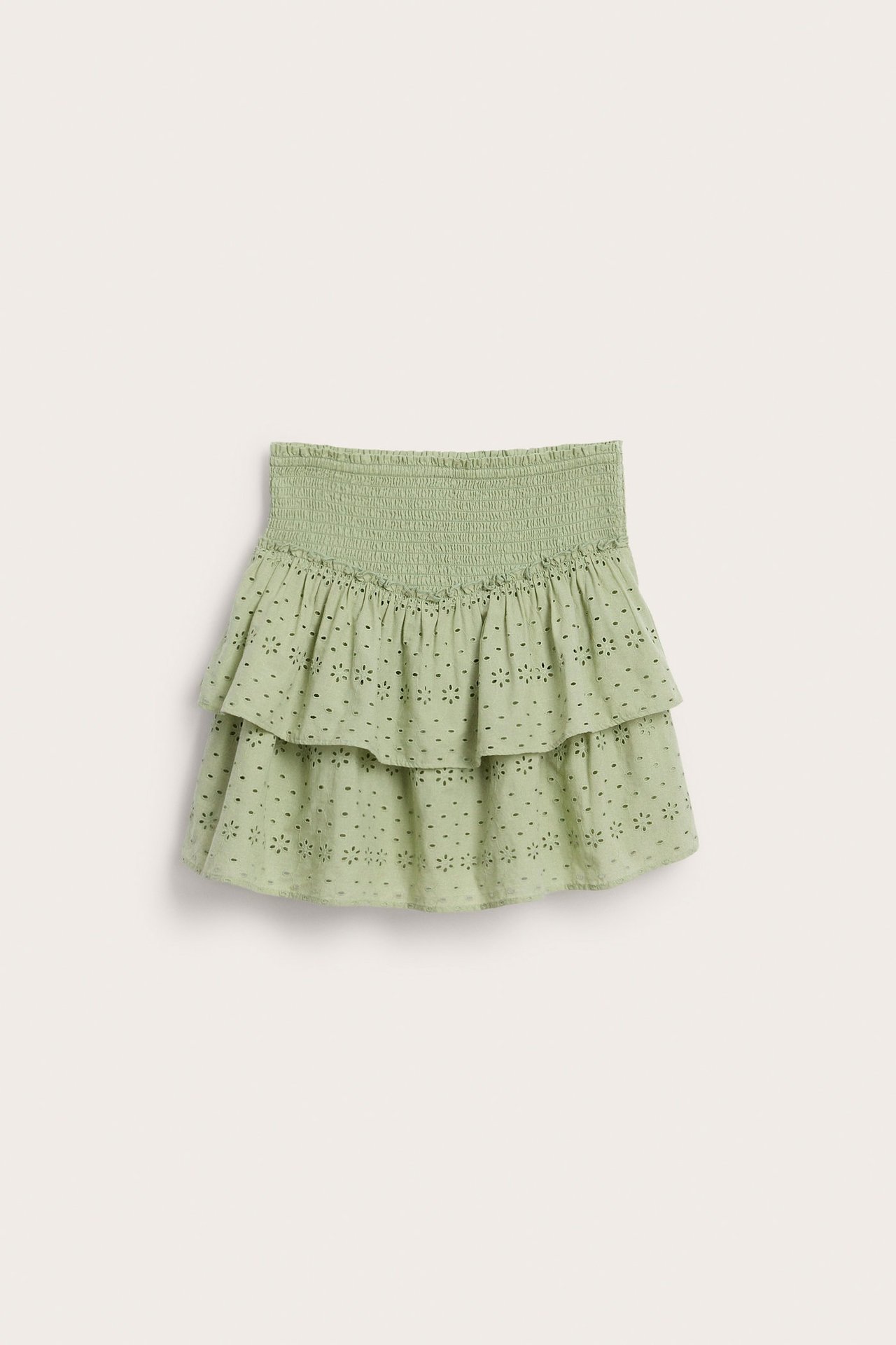 Edestäpäin, tummanvihreä lyhyt röyhelöhame, jossa smock-vyötärö ja broderie anglaise -kukkakuvio.