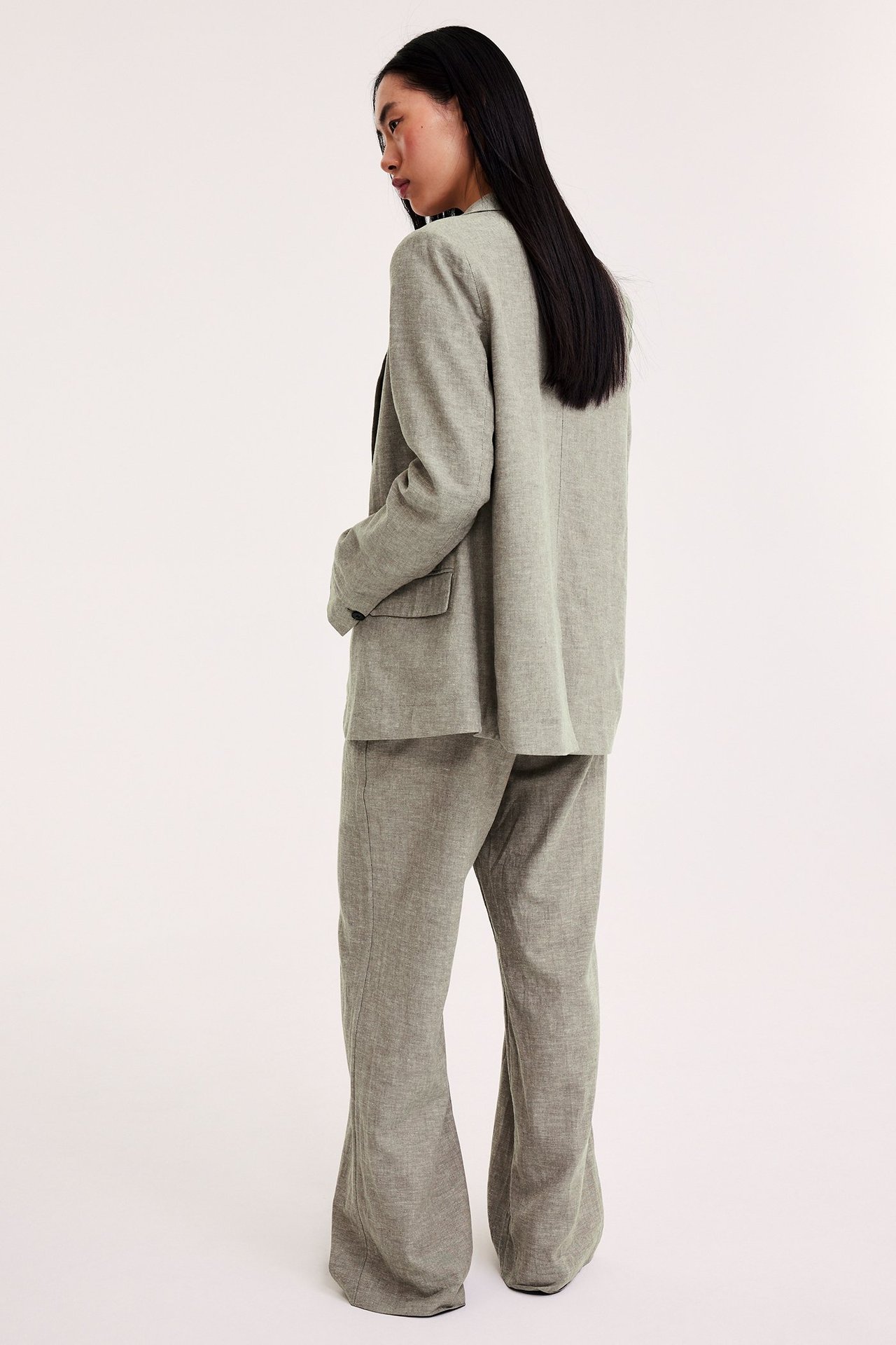 Bakifrån: kvinna i vida bruna melerade linnebyxor och en matchande kavaj.