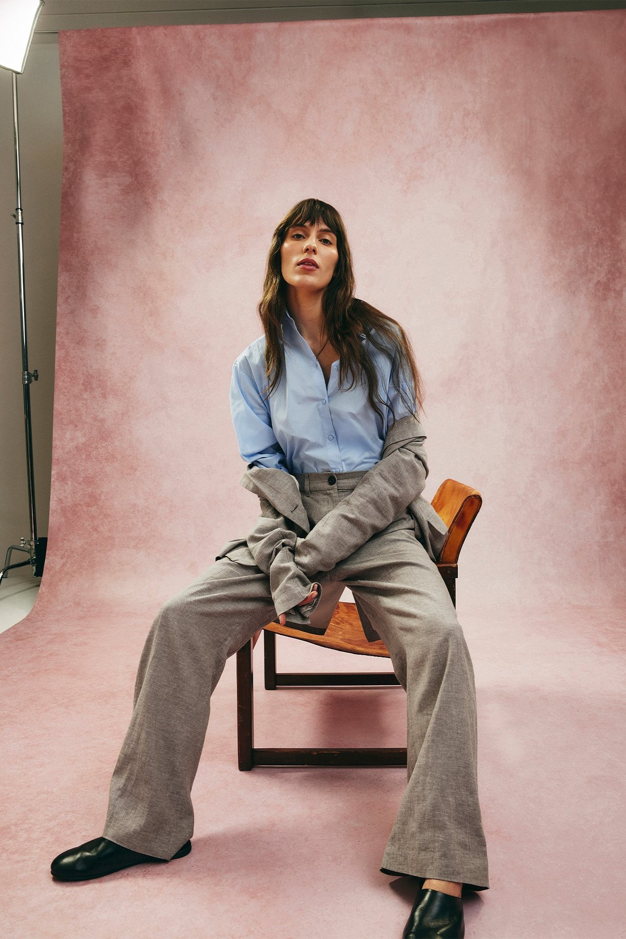 Framifrån: Kvinna i bruna melerade kostymbyxor i linnemix, en ljusblå skjorta och en grå kavaj draperad.