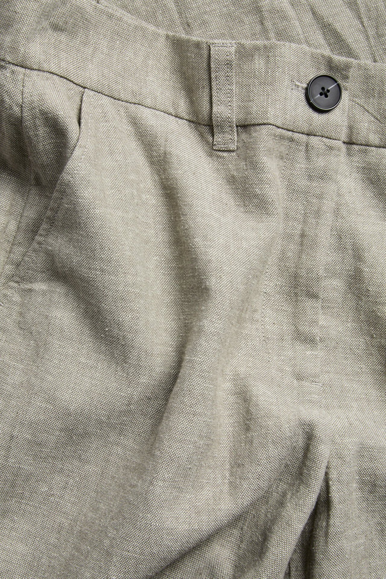 Lähikuva edestä melange ruskeista pellavasekoitepuvun housuista, joissa musta nappikiinnitys ja vyölenkit.