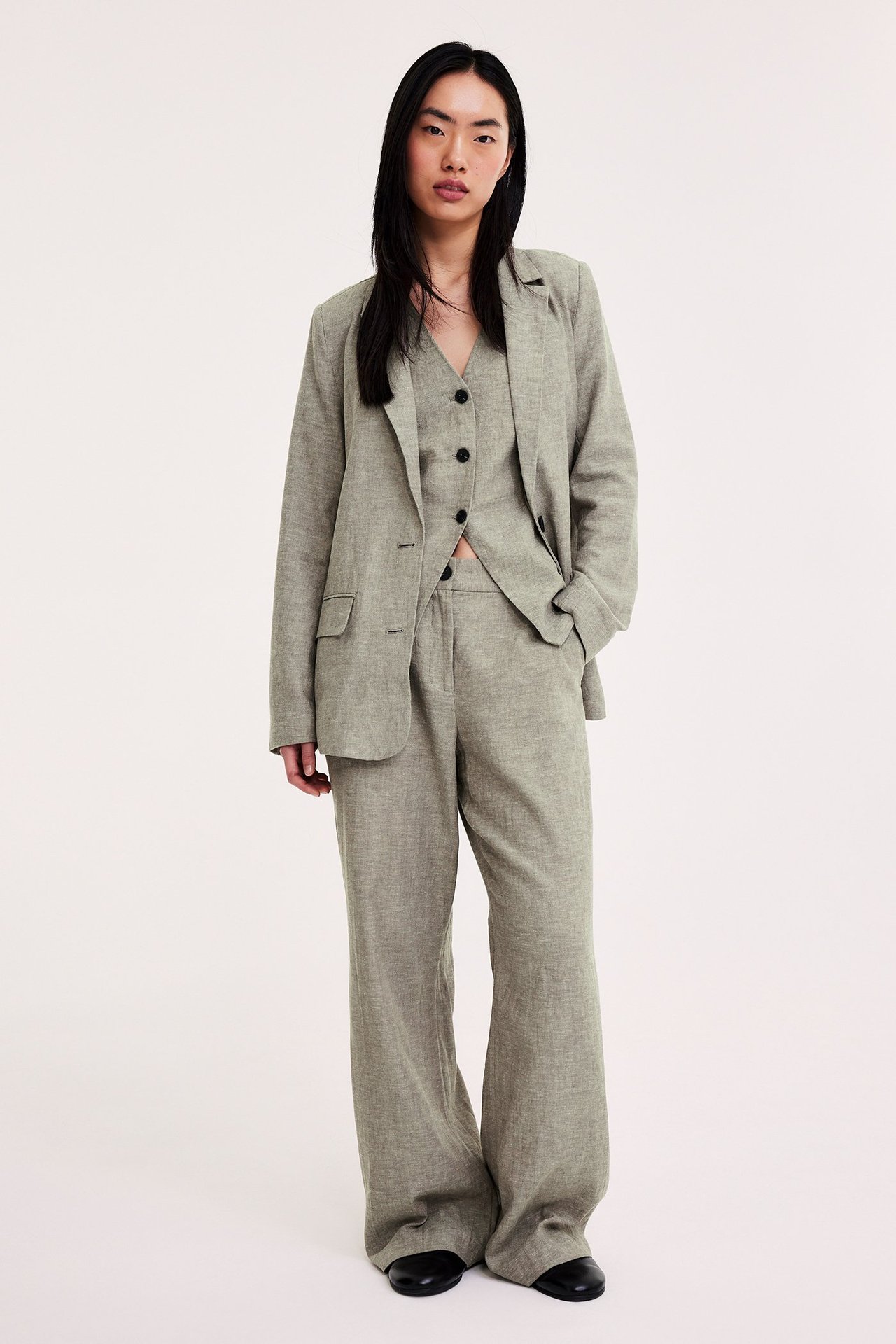 Etunäkymä: Nainen yllään kirjavanvihreät pellavasekoitehousut, yhteensopiva liivi ja avoin bleiseri.