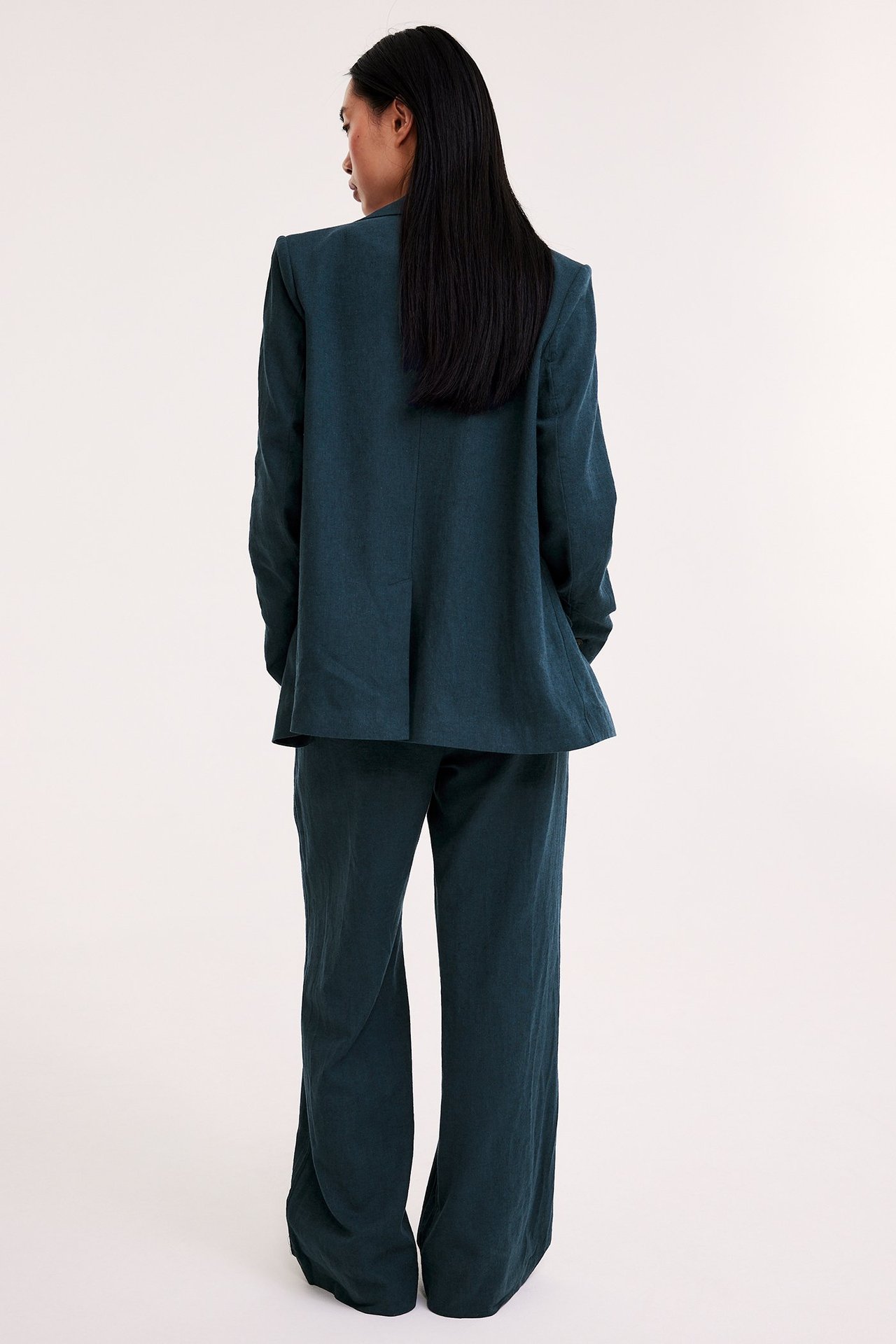 Ryggvy av en kvinna i mörkblå melerade kostymbyxor i linneblandning och matchande kavaj.