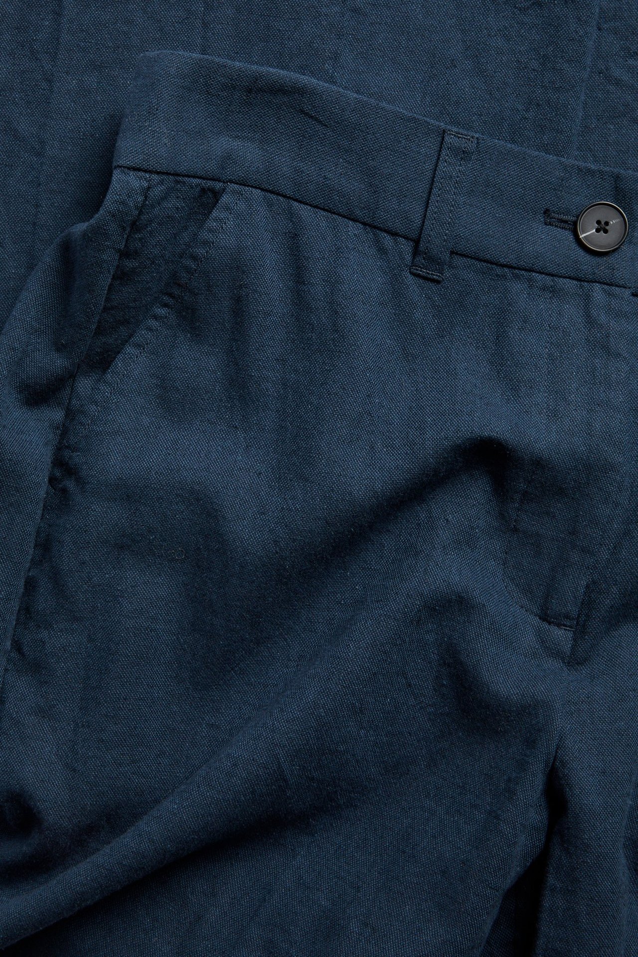 Lähikuva edestä tummansinisistä meleeratuista pellavasekoitepukuhousuista, joissa on nappikiinnitys.